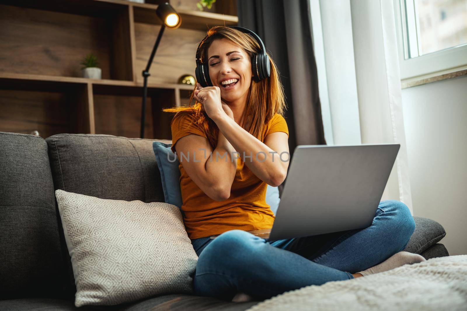 Shot of a young woman sitting cross legged on the sofa, dancing and listening music at home.