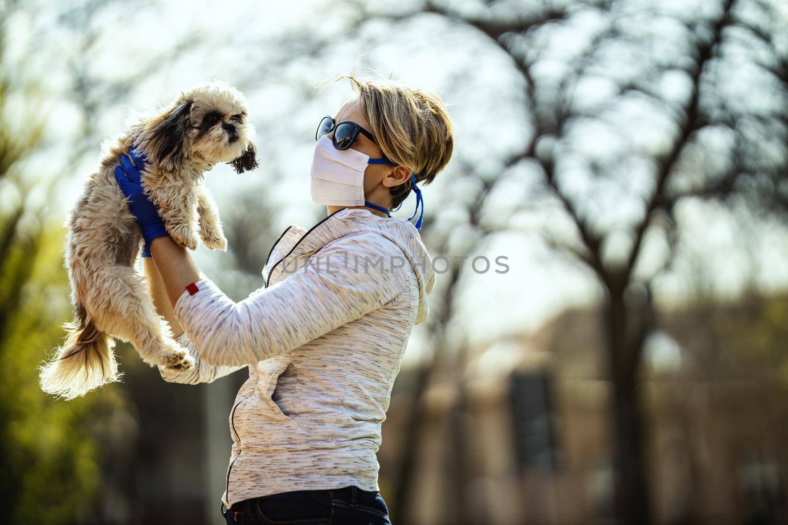 A woman in a medical protective mask is spending time with her dear cute little Shih Tzu dog on the city street path during flu virus outbreak and coronavirus epidemic.