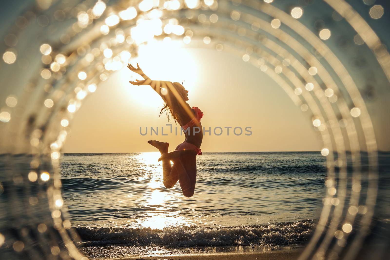 A beautiful creative composition of a sea landscape shot through a circle focus showing a teenage girl who having fun on the beach in sunset.