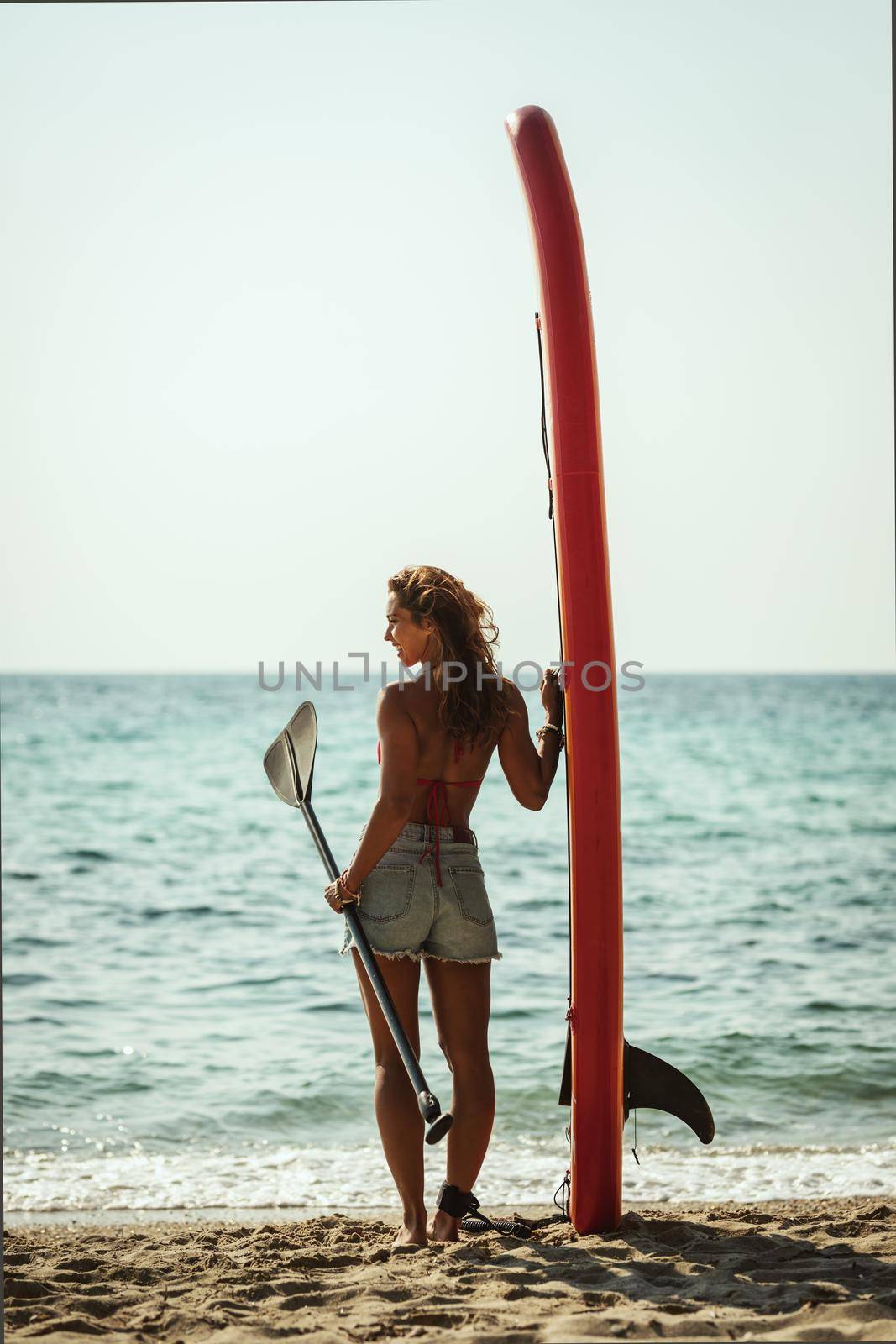 A young woman on a sea beach with a surfboard is ready for the waves.