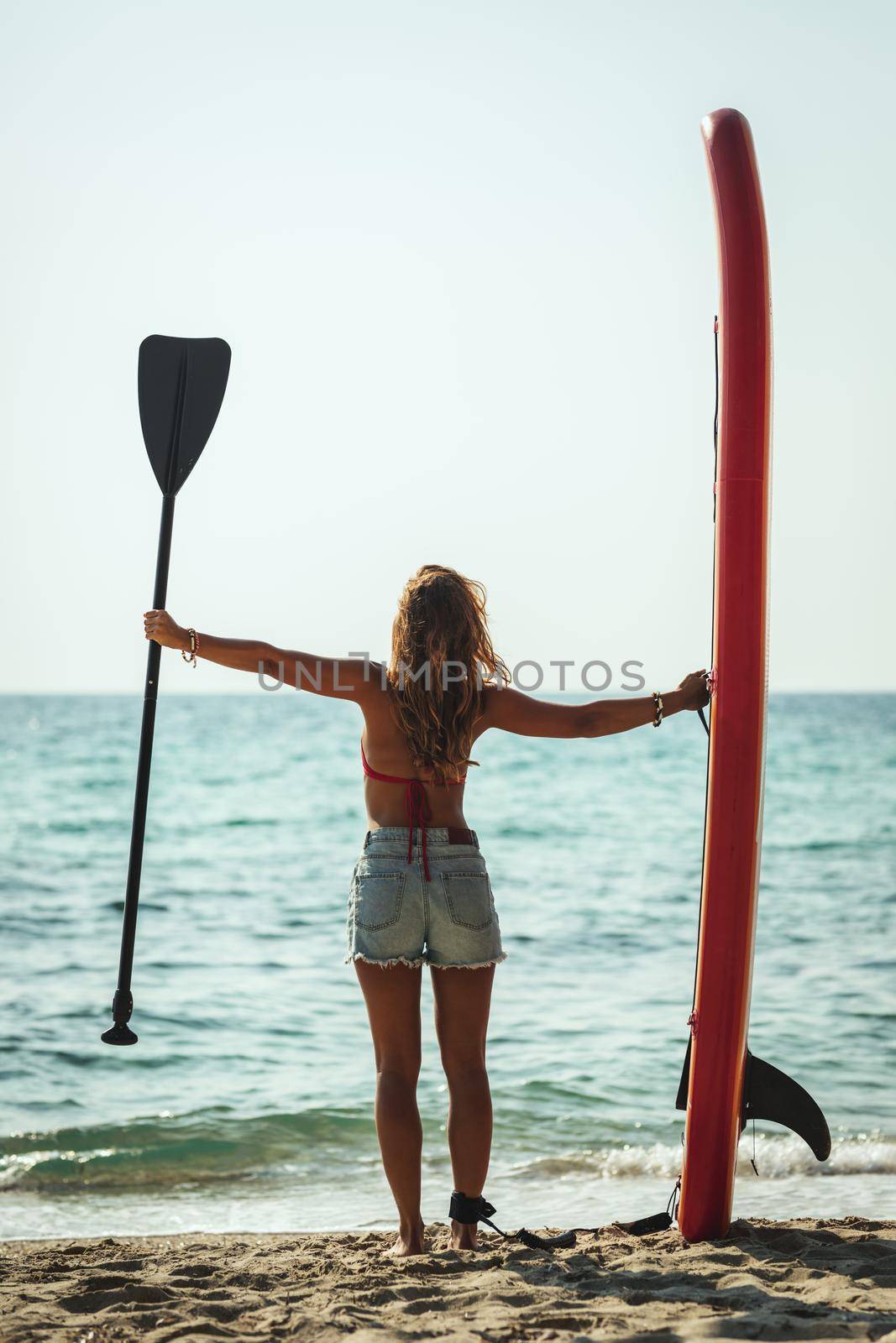 A young woman on a sea beach with a surfboard is ready for the waves.
