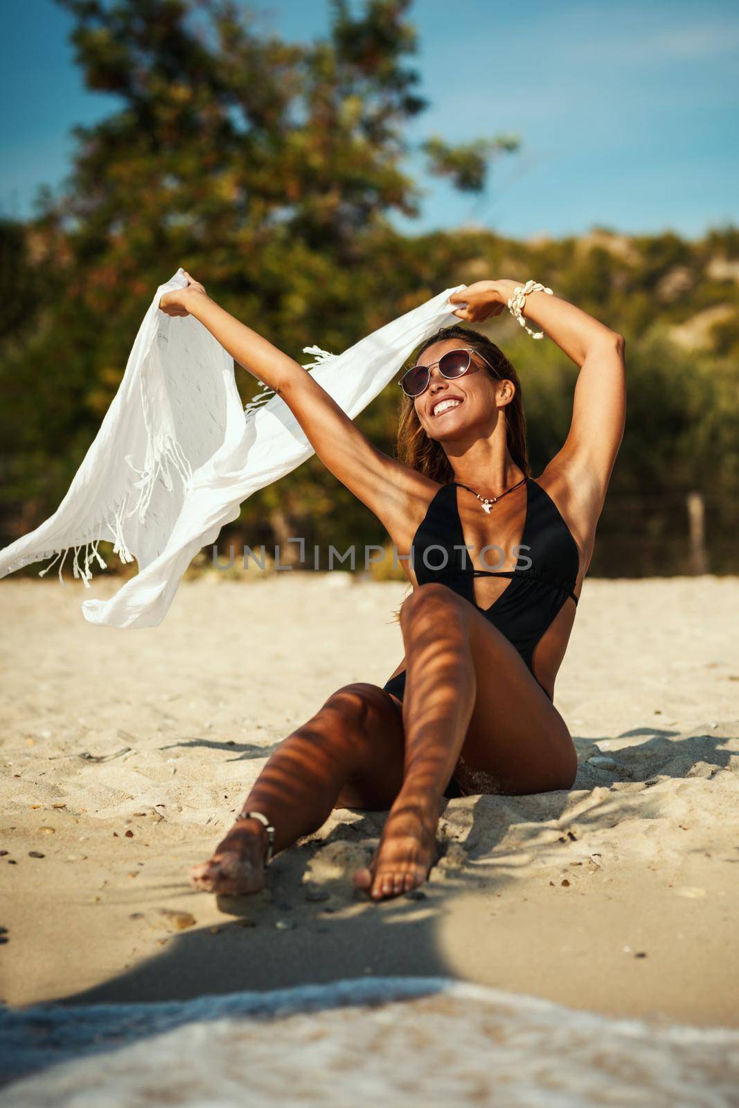 Attractive young woman is enjoying on the beach and holding up a linen cloth as the wind catches it.