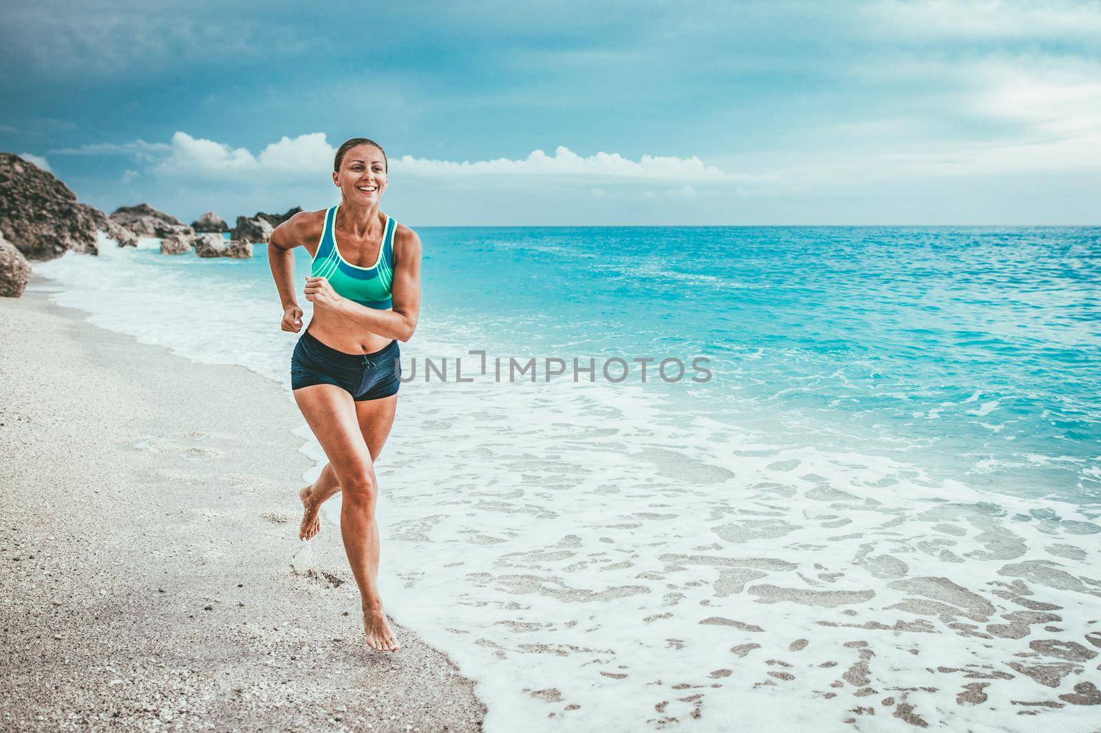 Beautiful young woman is running along the sea shore in the end of the day.