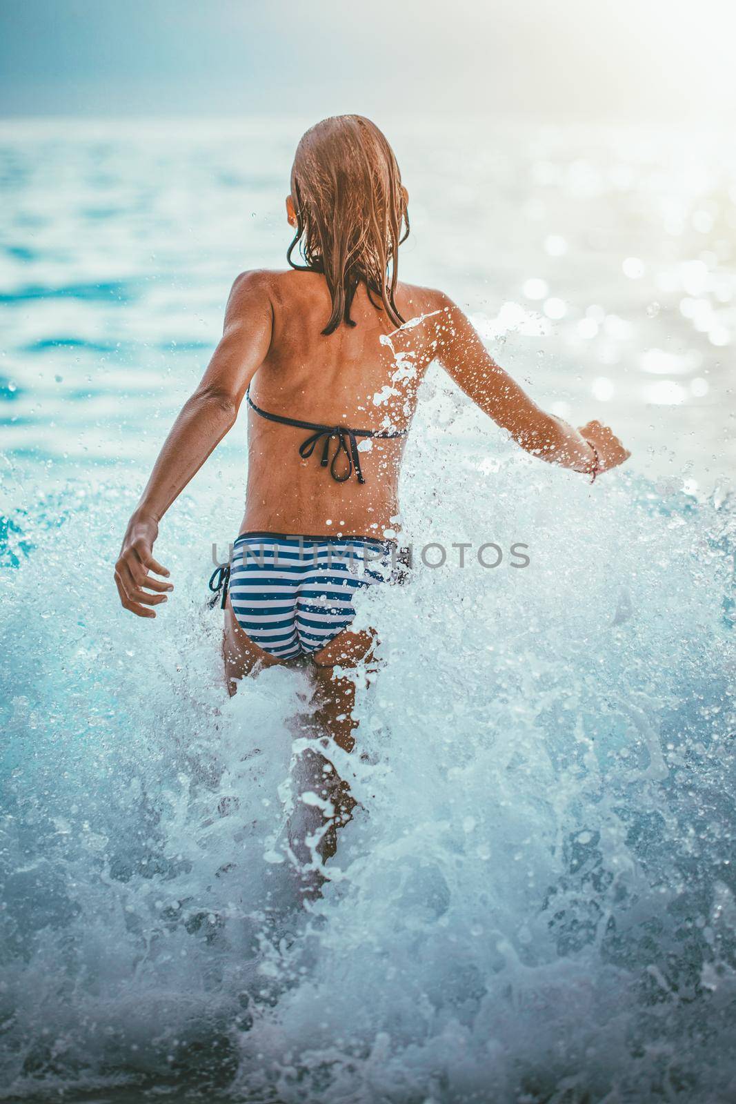 A little girl having fun in the waves of the sea and the drops of water are splashing all over her.
