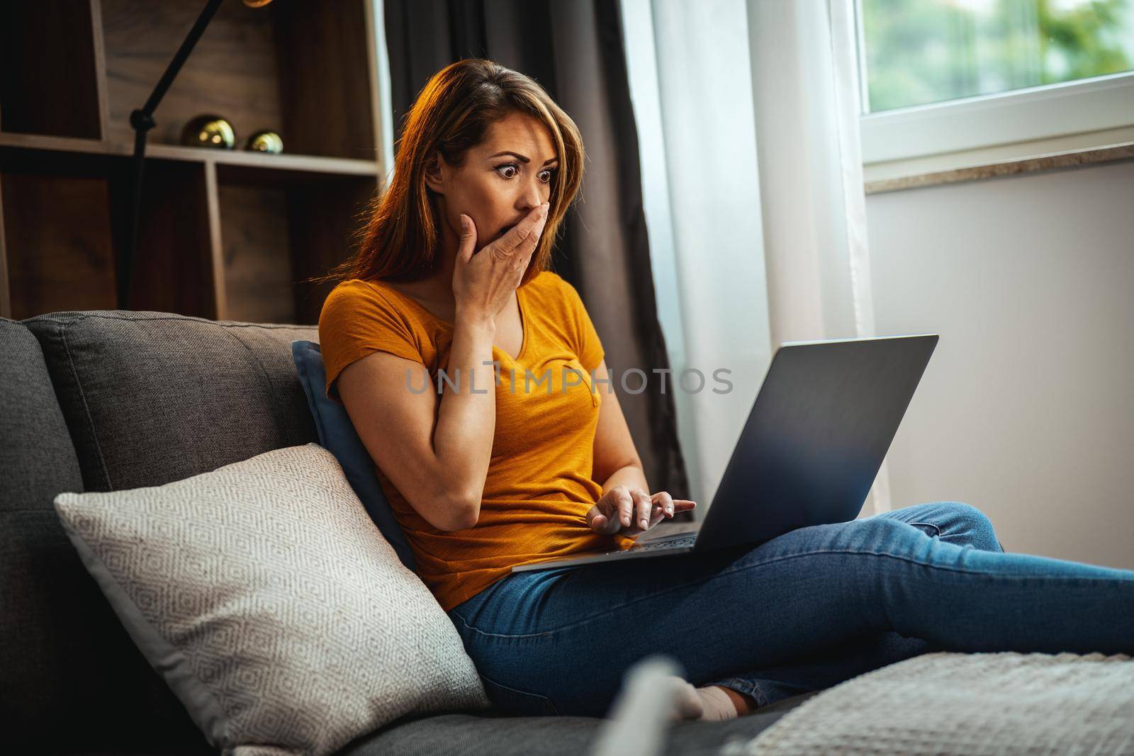 Shot of an surprised young woman while sitting on the sofa and using her laptop at home.