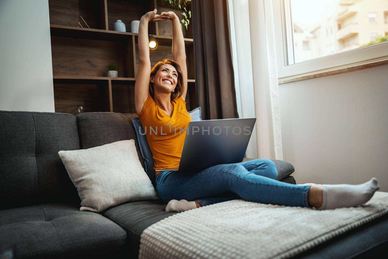 Beautiful young woman sitting on the sofa, enjoying and using her laptop at home.