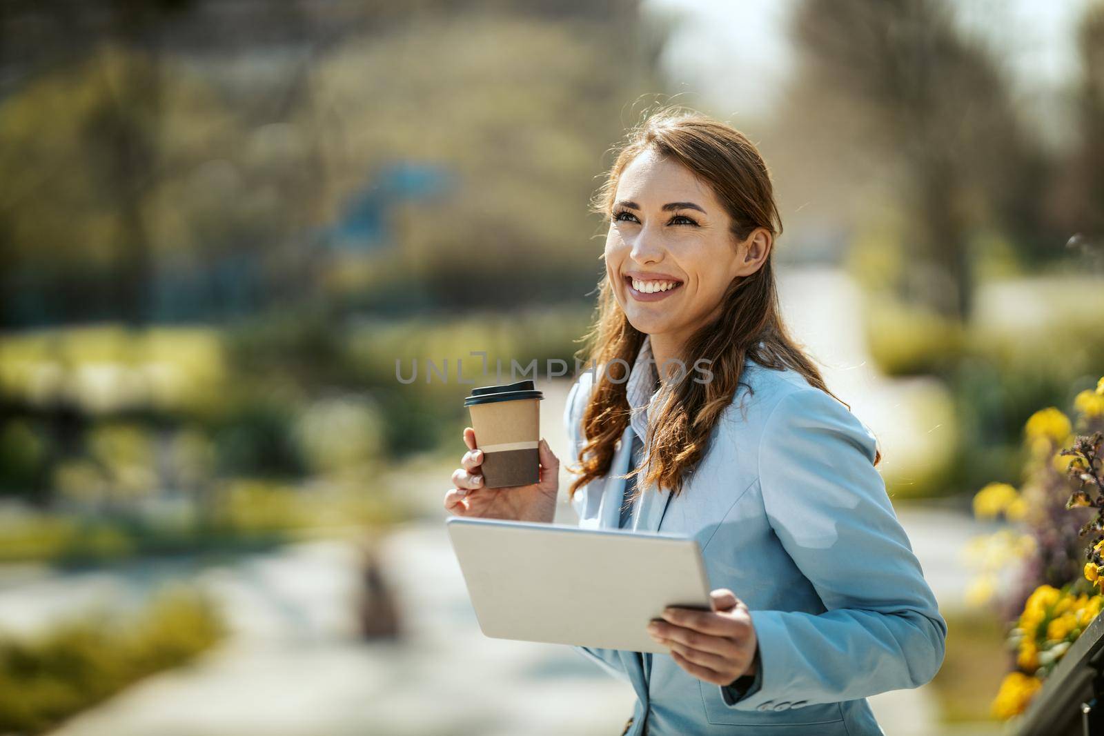 Young smiling businesswoman with tablet in her hands is standing in front of office during coffee break.