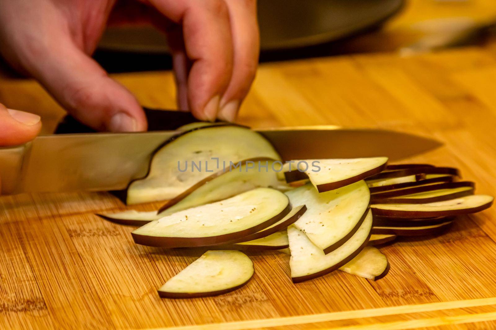 The cook cuts an eggplant on a cutting board. The process of preparing a vegetable dish. Unrecognizable person. by Milanchikov