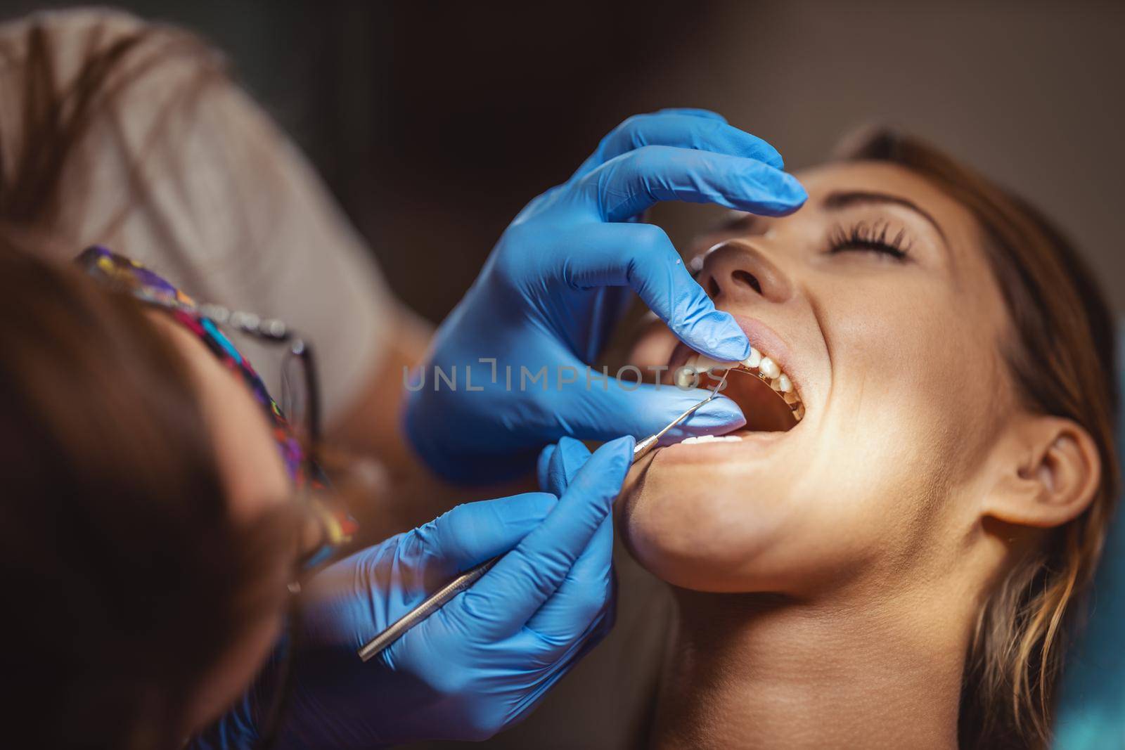 The beautiful young woman is at the dentist. She sits in the dentist's chair and the dentist sets braces on her teeth putting aesthetic self-aligning lingual locks.