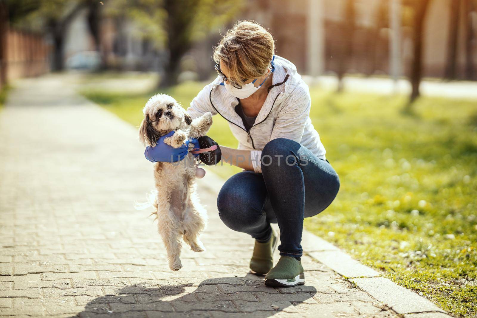 A woman in a medical protective mask is spending time and walking with her cute little Shih Tzu dog during allergy or flu virus outbreak and coronavirus epidemic.