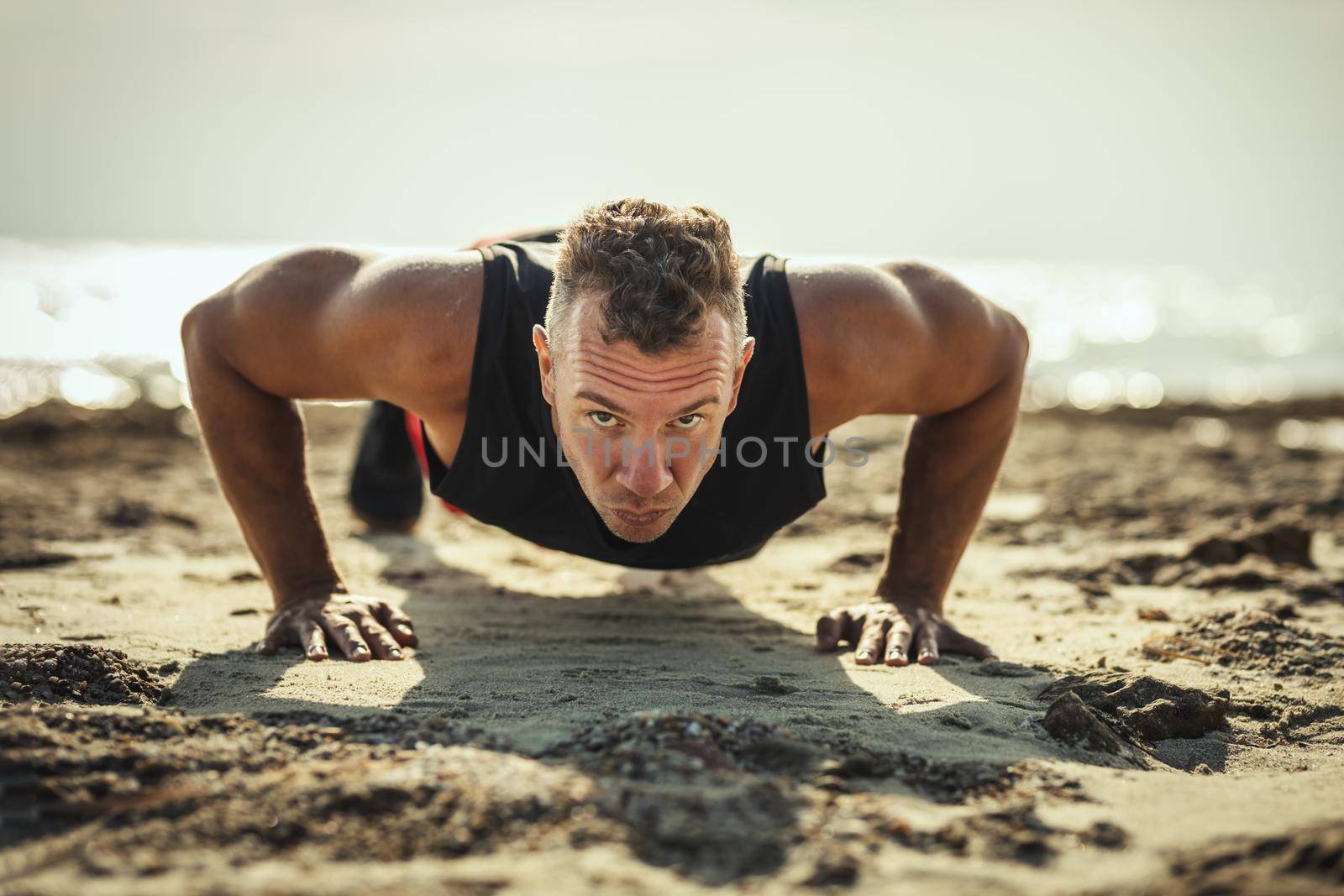 A handsome man is doing push-up exercise at the sea beach in summer sunny day.