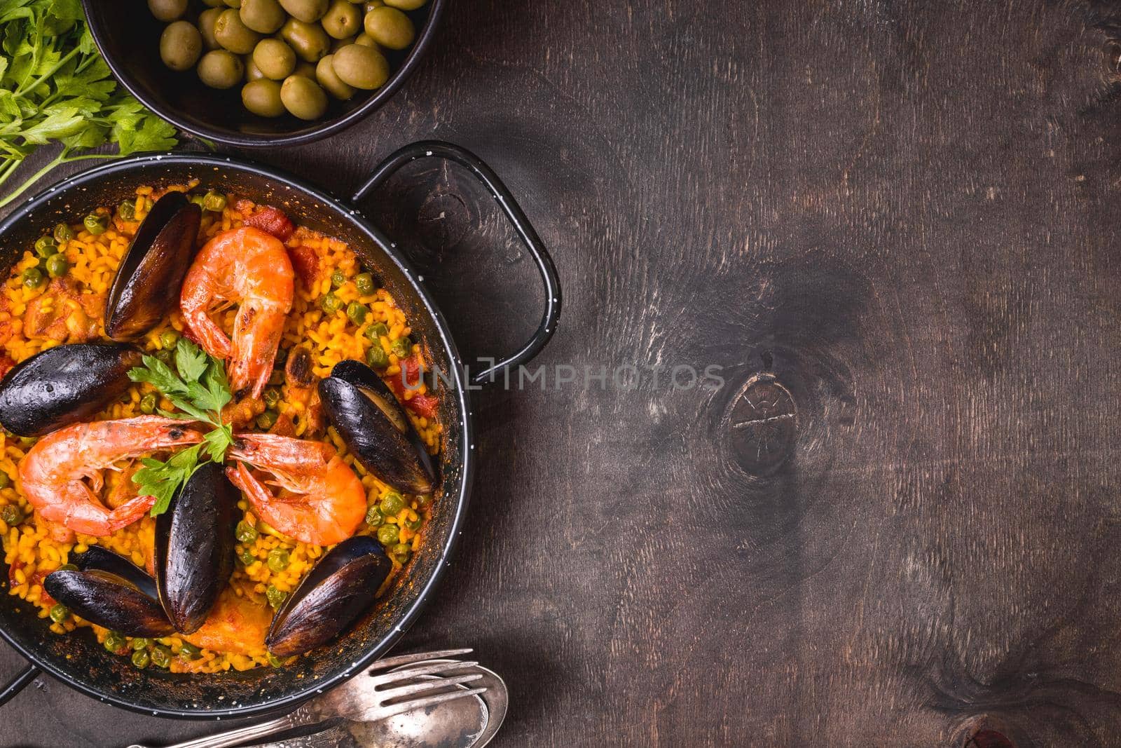 Paella background, space for text. Paella in black pan with saffron rice, peas, shrimps, mussels, squid, meat. Seafood paella, traditional spanish dish. Paella on rustic black wooden table. Top view