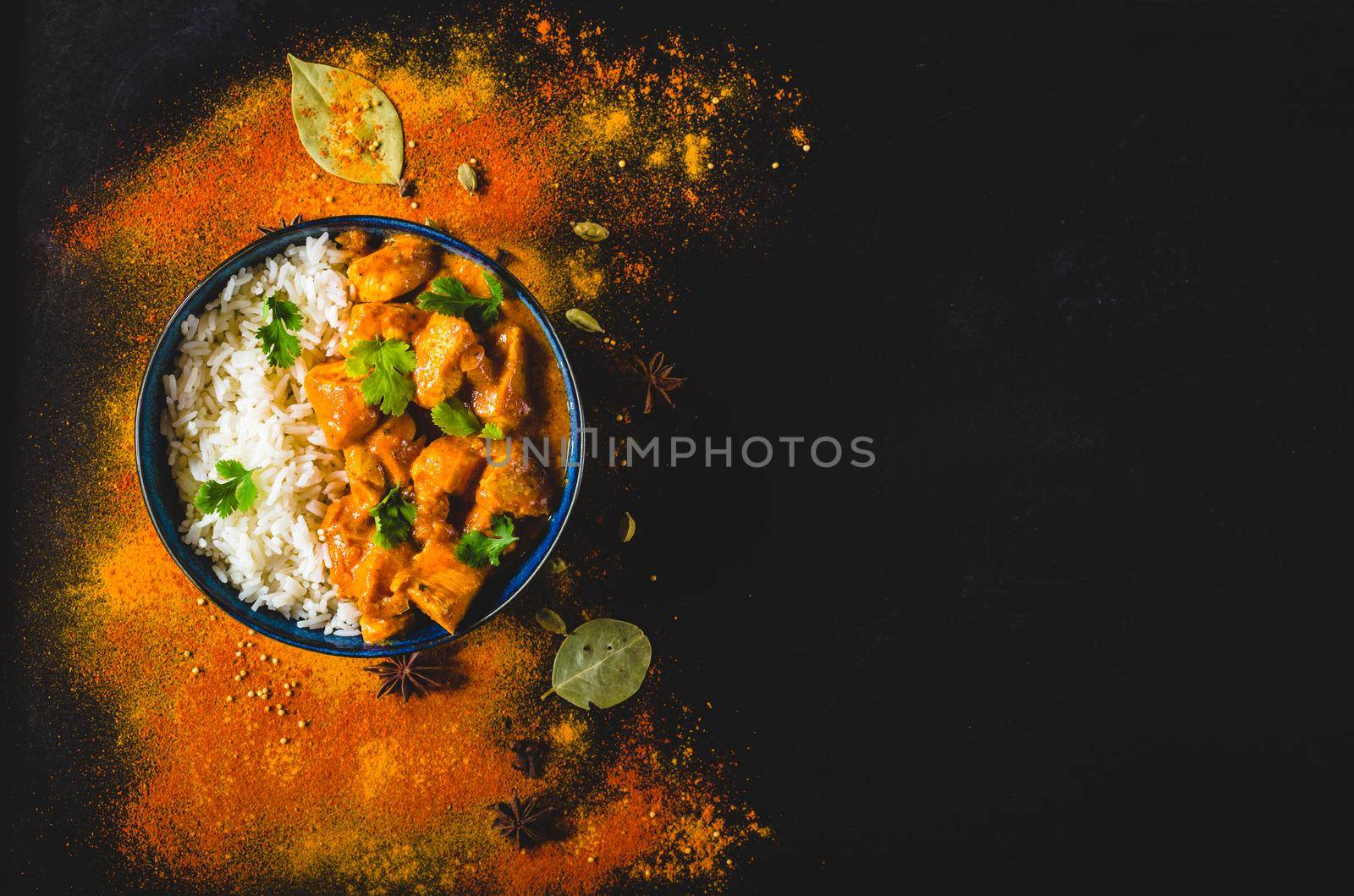 Indian Butter chicken with basmati rice in bowl, spices, black background. Space for text. Butter chicken, traditional Indian dish. Top view. Chicken tikka masala. Indian cuisine concept. Overhead