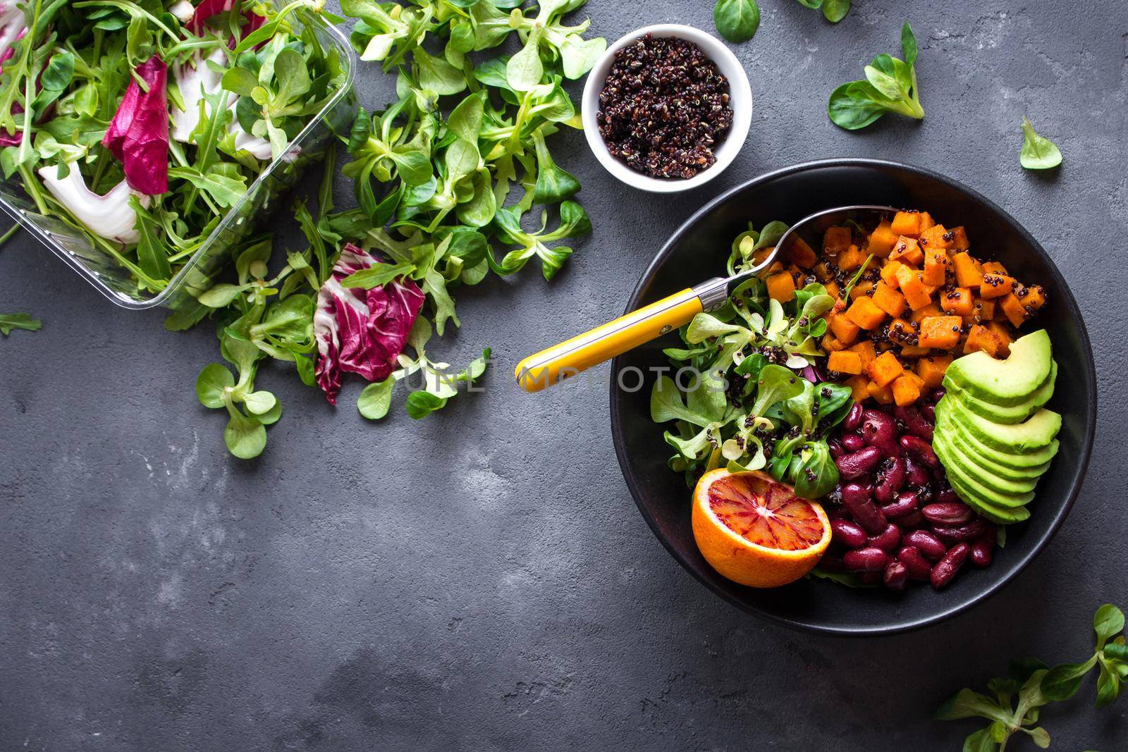 Quinoa salad in bowl with avocado, sweet potato, beans, herbs, orange on concrete rustic background. Quinoa superfood concept. Clean healthy detox eating. Vegan/vegetarian food. Making healthy salad