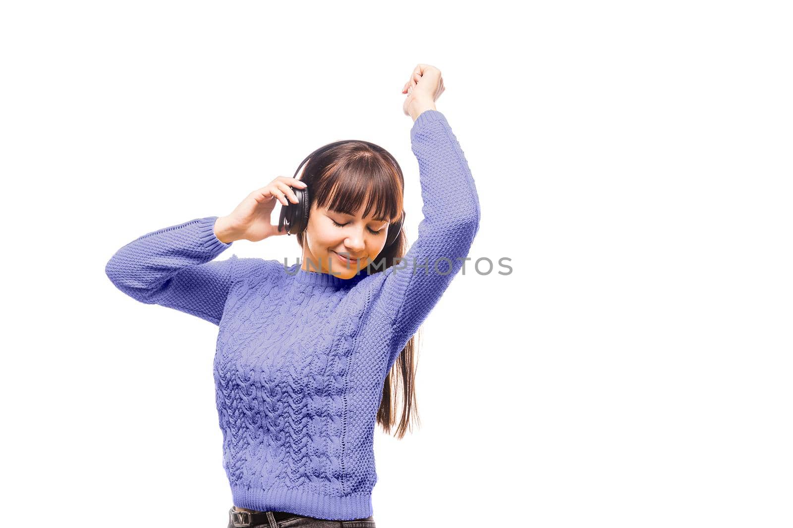 A brunette woman in a violet sweater is listening to music with headphones. Demonstrating the colors of 2022 - Very Peri.