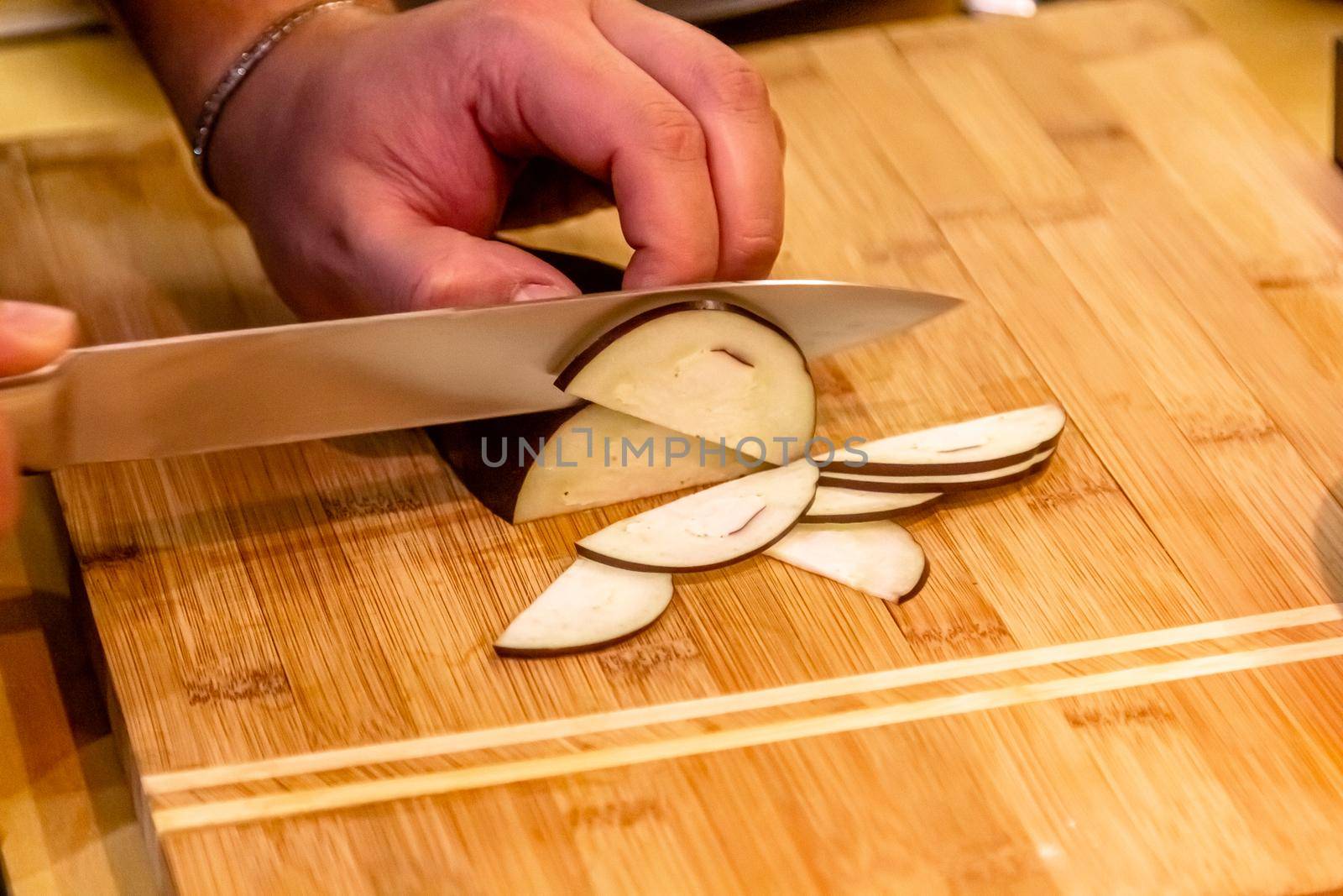 The cook cuts an eggplant on a cutting board. The process of preparing a vegetable dish. Unrecognizable person. Close-up
