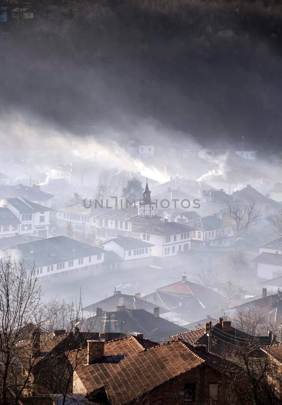 Mountain town in clouds of fog and smoking chimneys early morning