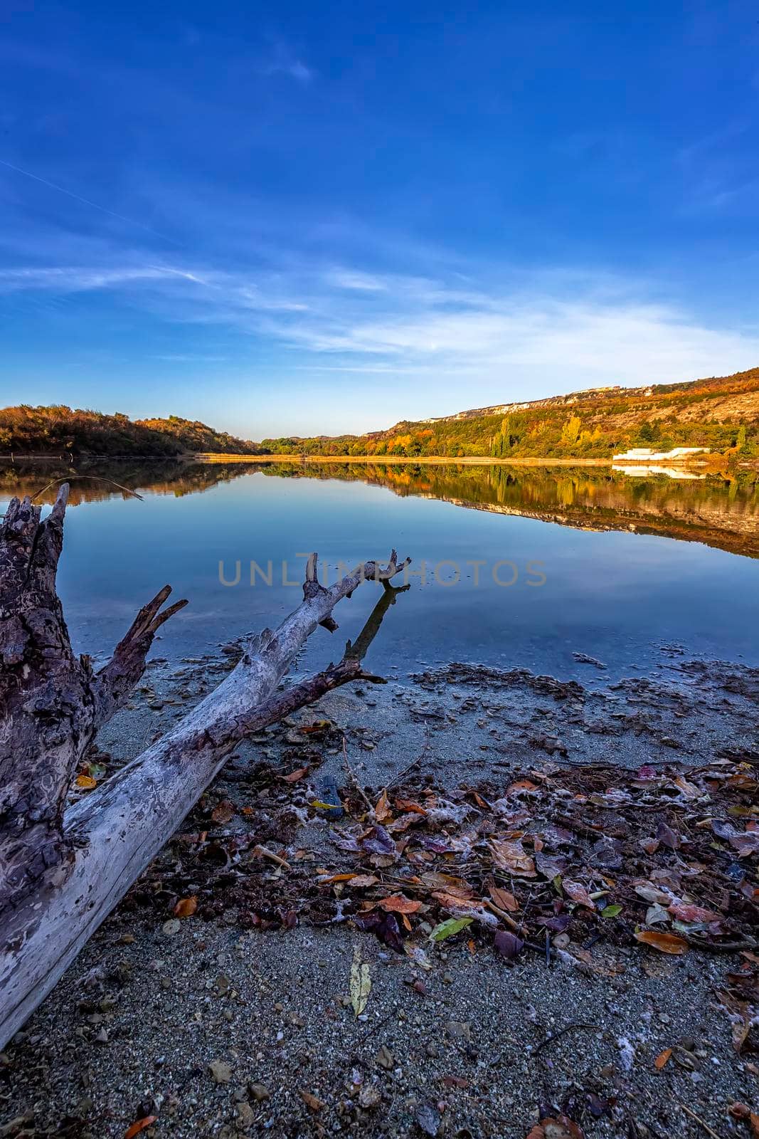 Vertical view from the shore of old and mountain hills with autumn colors reflected in still lake water  by EdVal