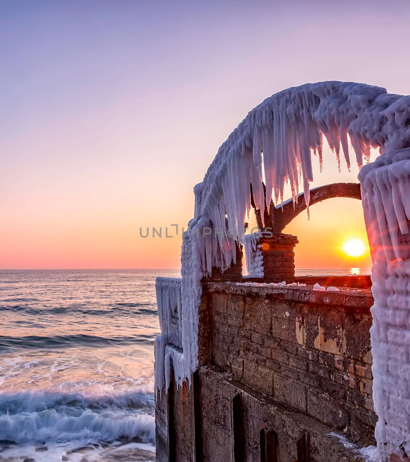 Winter sea view of a frozen fence and sun between ice window. Concept