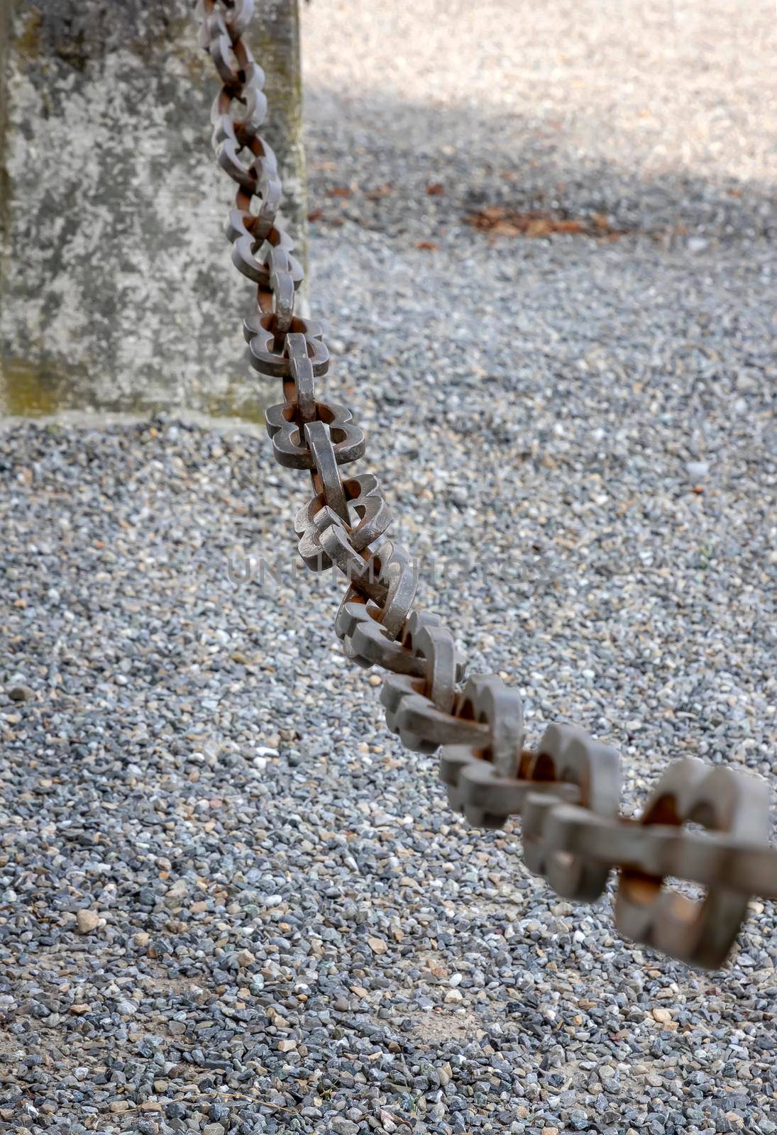 A light gray metal chain made of steel and showing its age is seen up close as it hangs above the broken stone ballast. Selective focus.
