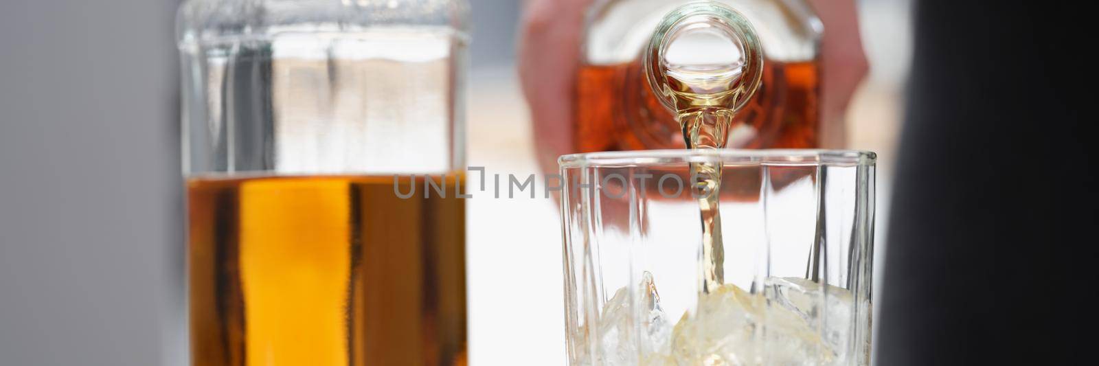 A man pours a strong alcoholic drink into a glass with ice, close-up. Whiskey in a wide glass with a thick bottom, calvados in a decanter