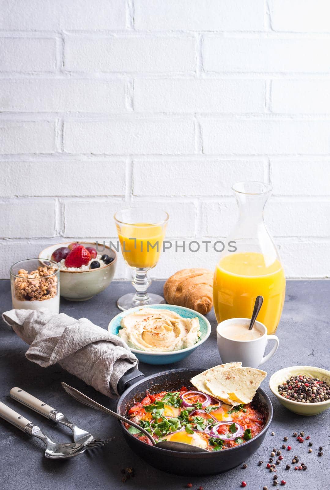 Big healthy breakfast with middle eastern and european food. Shakshuka eggs, pita, hummus, cottage cheese, fruits, yogurt, granola, croissant, coffee, juice. international breakfast. Selective focus.