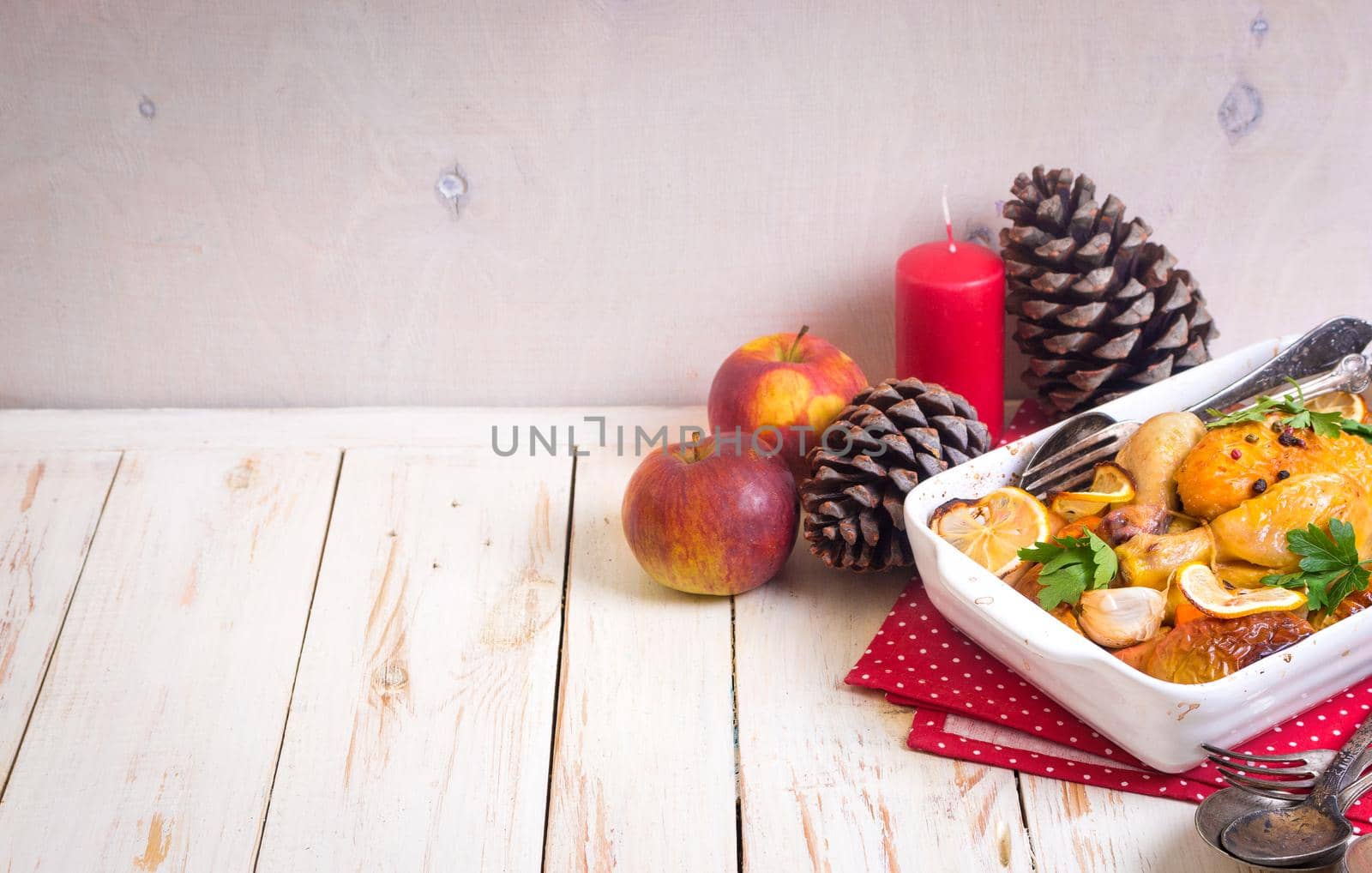 Roasted chicken. Christmas food background. Celebration white wooden table with roasted chicken, apples, decorated with candles, cones, vintage cutlery. Christmas/Thanksgiving dinner. Space for text