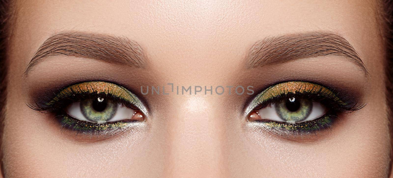 Closeup Macro of Woman Face with Green Eyes Make-up. Fashion Gold Autumn Makeup, Glowy Clean Skin, perfect Shapes of Brows. Shiny Shimmer. Beautiful Fall Trendy Colors in Make-up