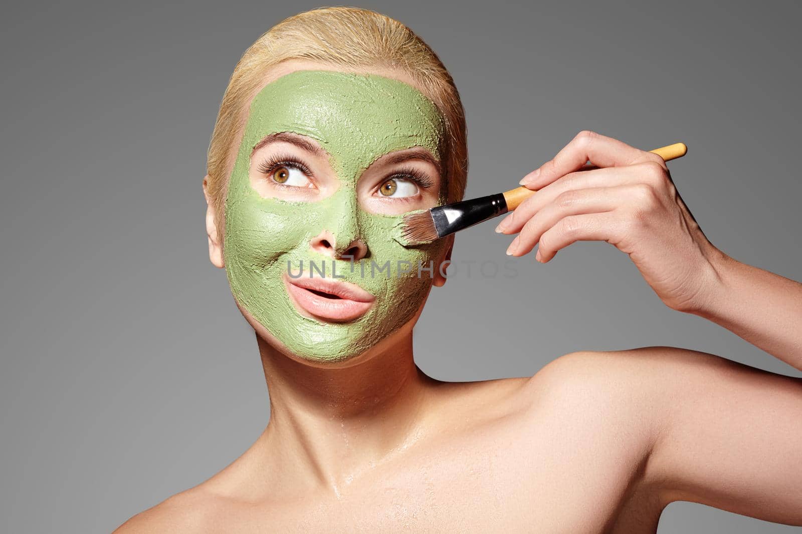 Beautiful Woman Applying Green Facial Mask. Beauty Treatments. Spa Girl Apply Clay Facial mask on grey background by MarinaFrost