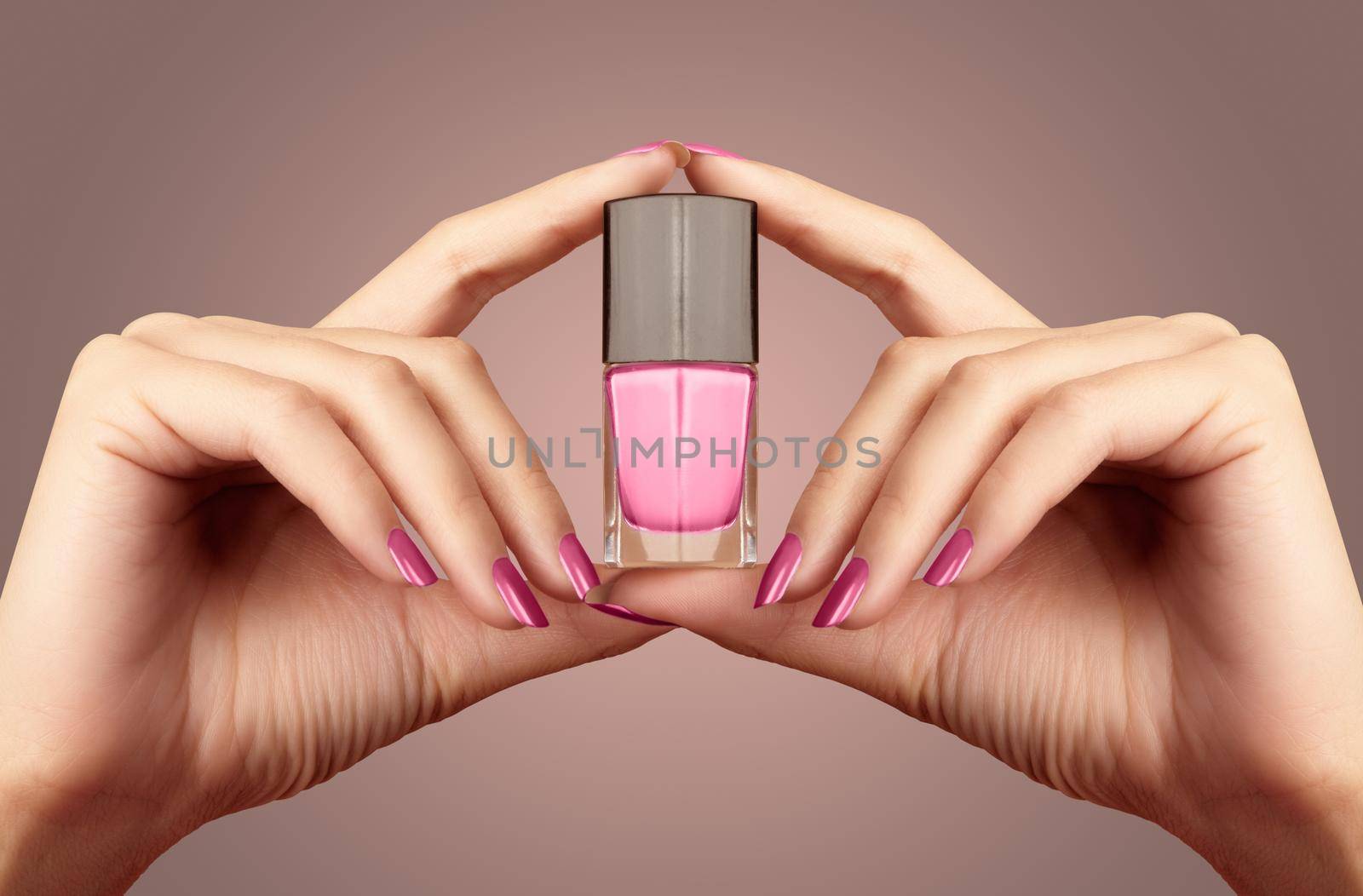 Manicured nails with pastel nail polish. Manicure with bright nailpolish. Fashion manicure. Shiny gel lacquer in bottle. Beautiful female hands with pink bottle on beige background