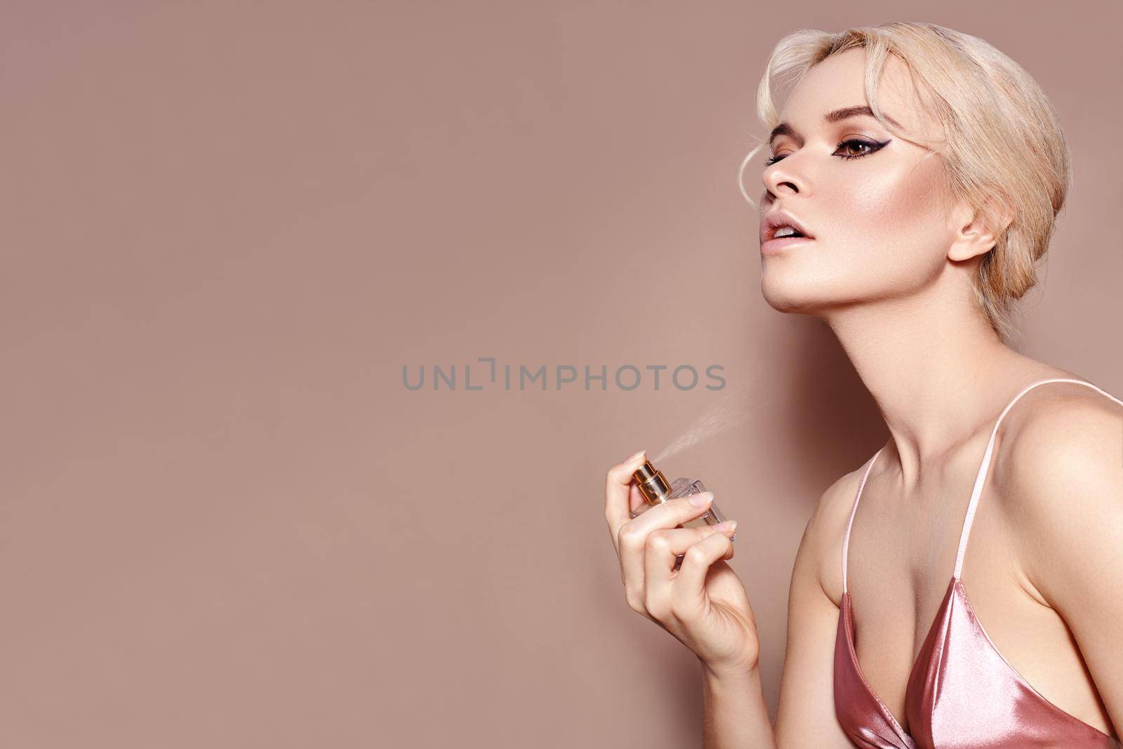 Beautiful Woman Applying Perfume Spray on neck. Blond Model with sexy Retro Make-up in Pink Lingerie Smells Fragrance by MarinaFrost