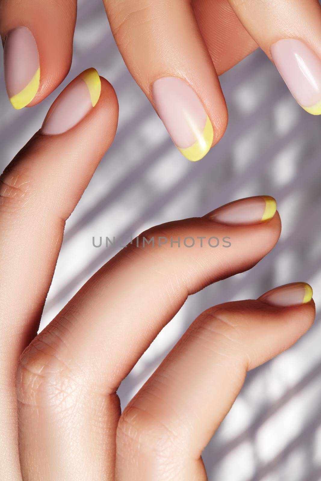 Hands with bright yellow french manicure on geometric background. Nails art design. Close-up of female hands with trendy neon nails on silver striped print