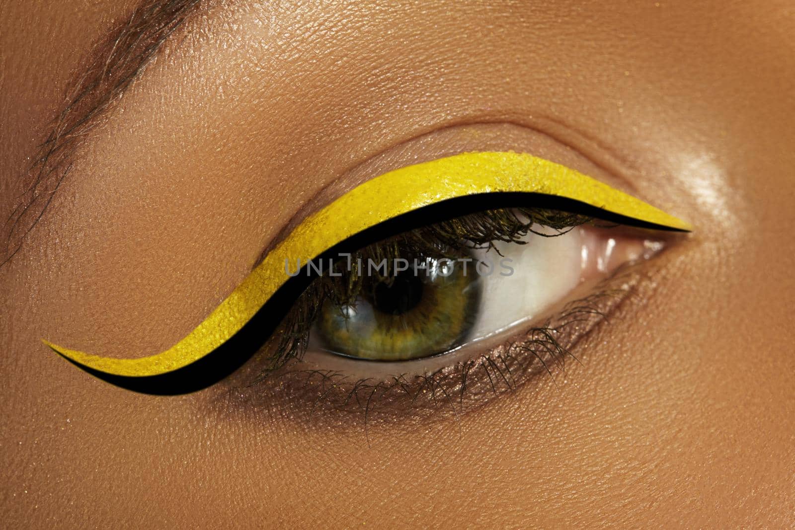 Beautiful macro close-up of female Eye with bright yellow Eyeliner Makeup. Neon Disco make-up with fashion black liner. Summer beauty style. Closeup macro shot of fashion liner eyes visage