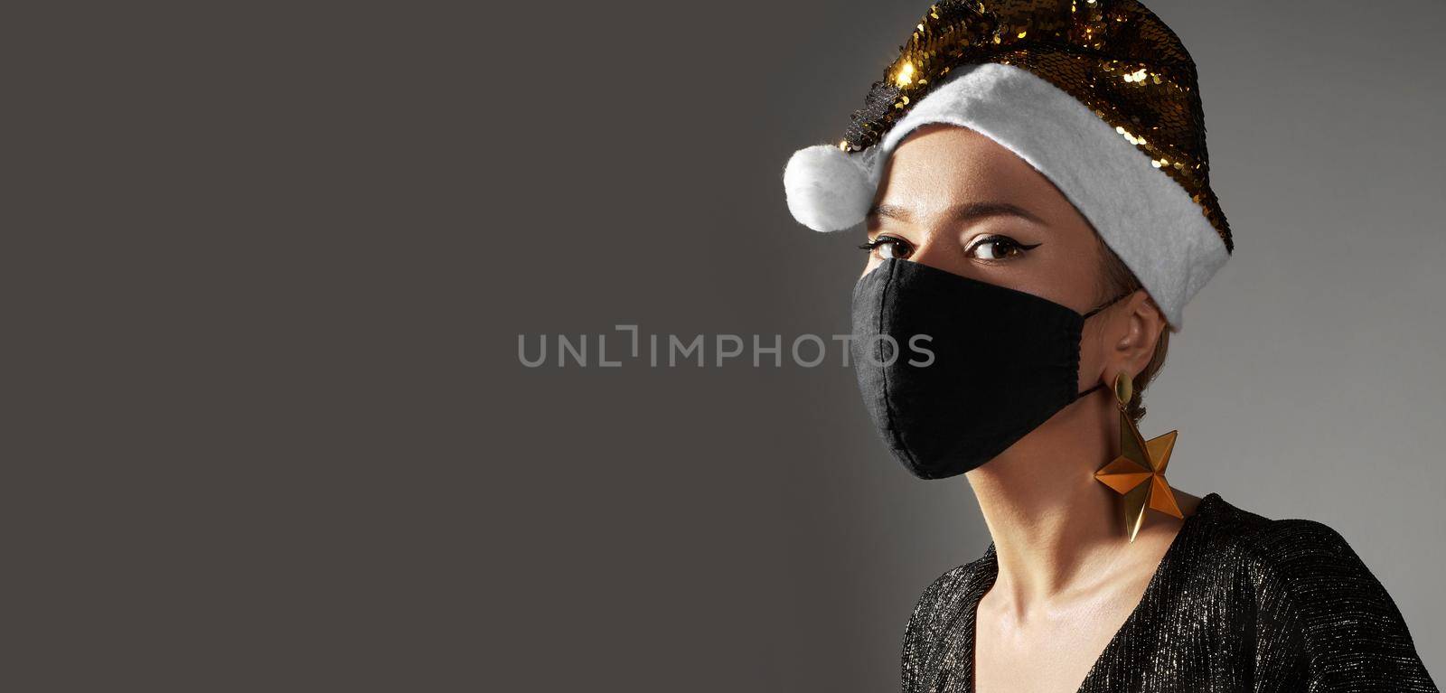 Woman with gold christmas hat, black medical mask. Fashion style with shiny clothes and accessories for xmas time. Protect yourself from Coronavirus Covid-19 even on holidays