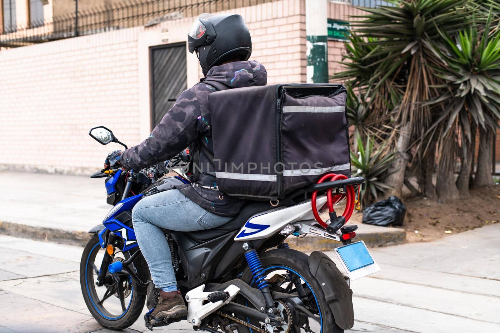 Food delivery driver with backpack on a motorcycle riding along a street. by Peruphotoart