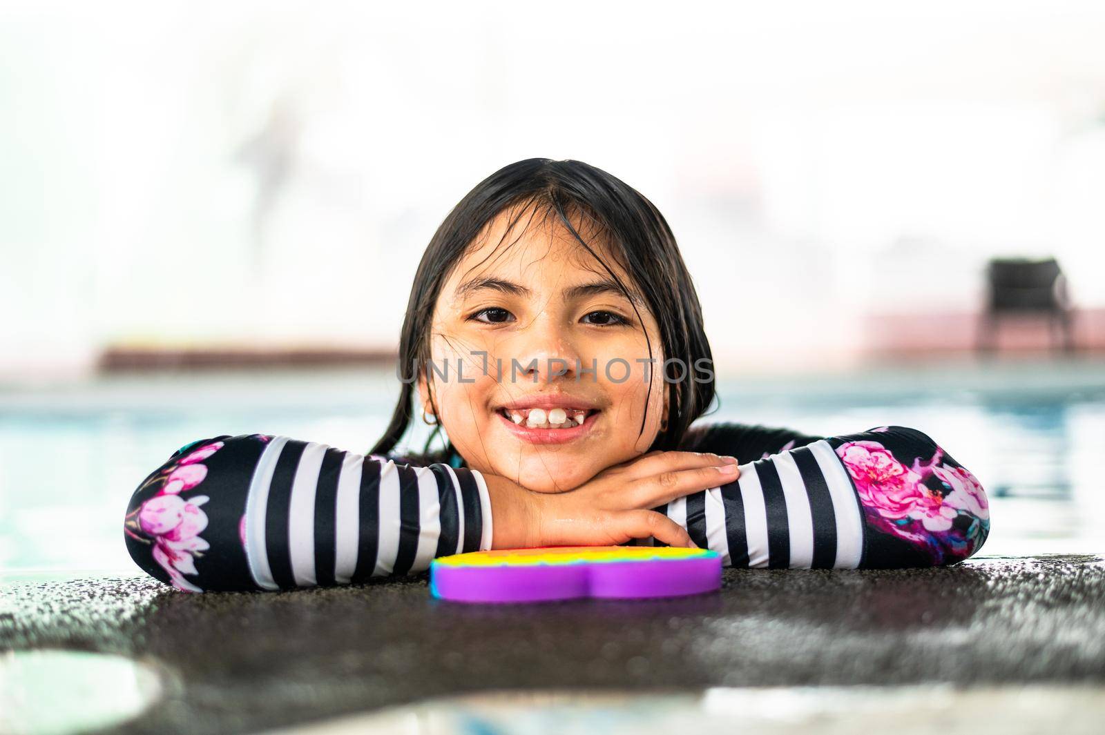 Portrait girl having fun in indoor swimming-pool. The girl is resting at the water park. Active happy kid. Swimming school for small children. Concept friendly family sport and summer vacation. by Peruphotoart