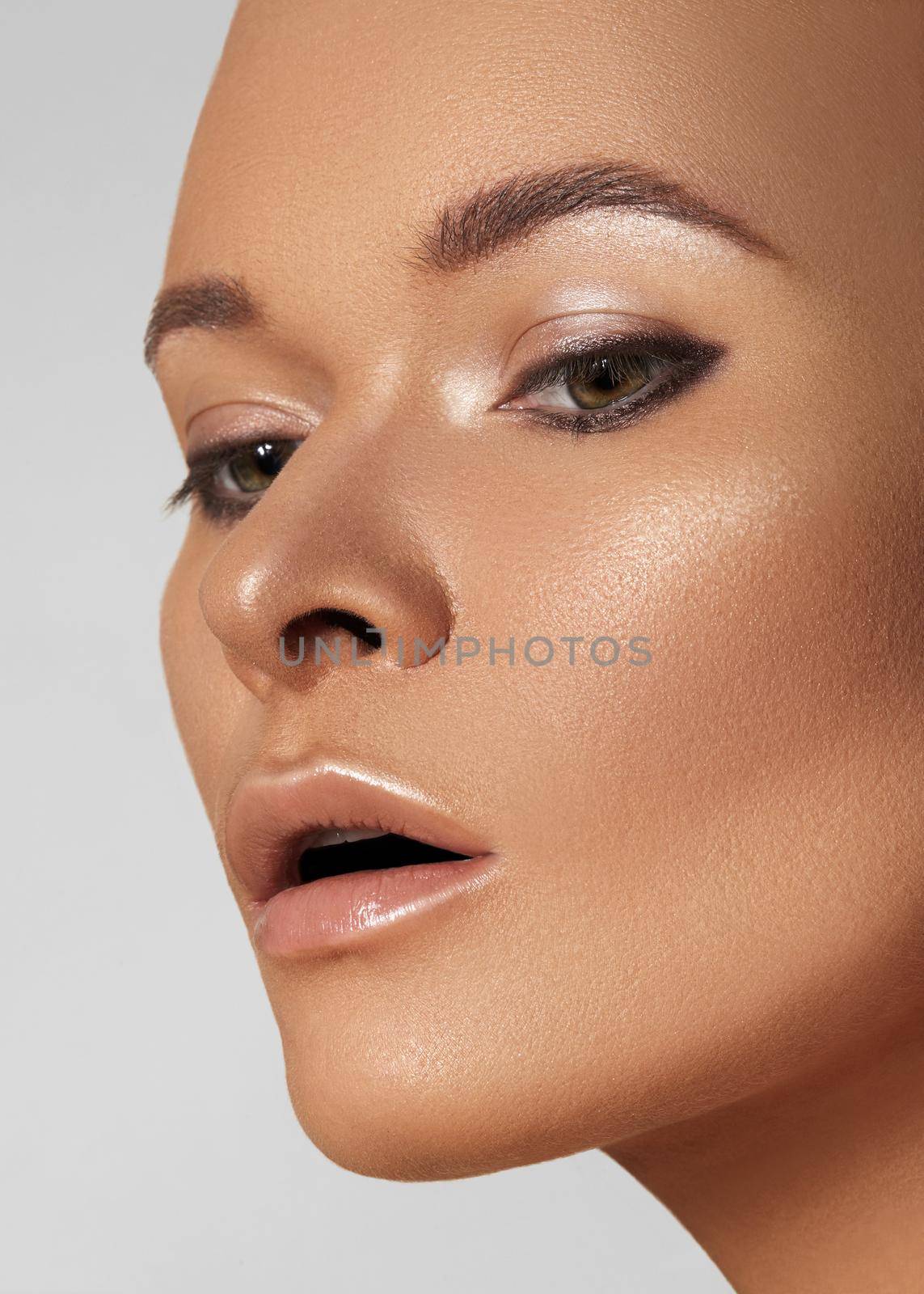 Close-up face of beautiful young woman with smooth tanned skin. Portrait of beauty model with natural bronze make-up. Spa, skincare and wellness