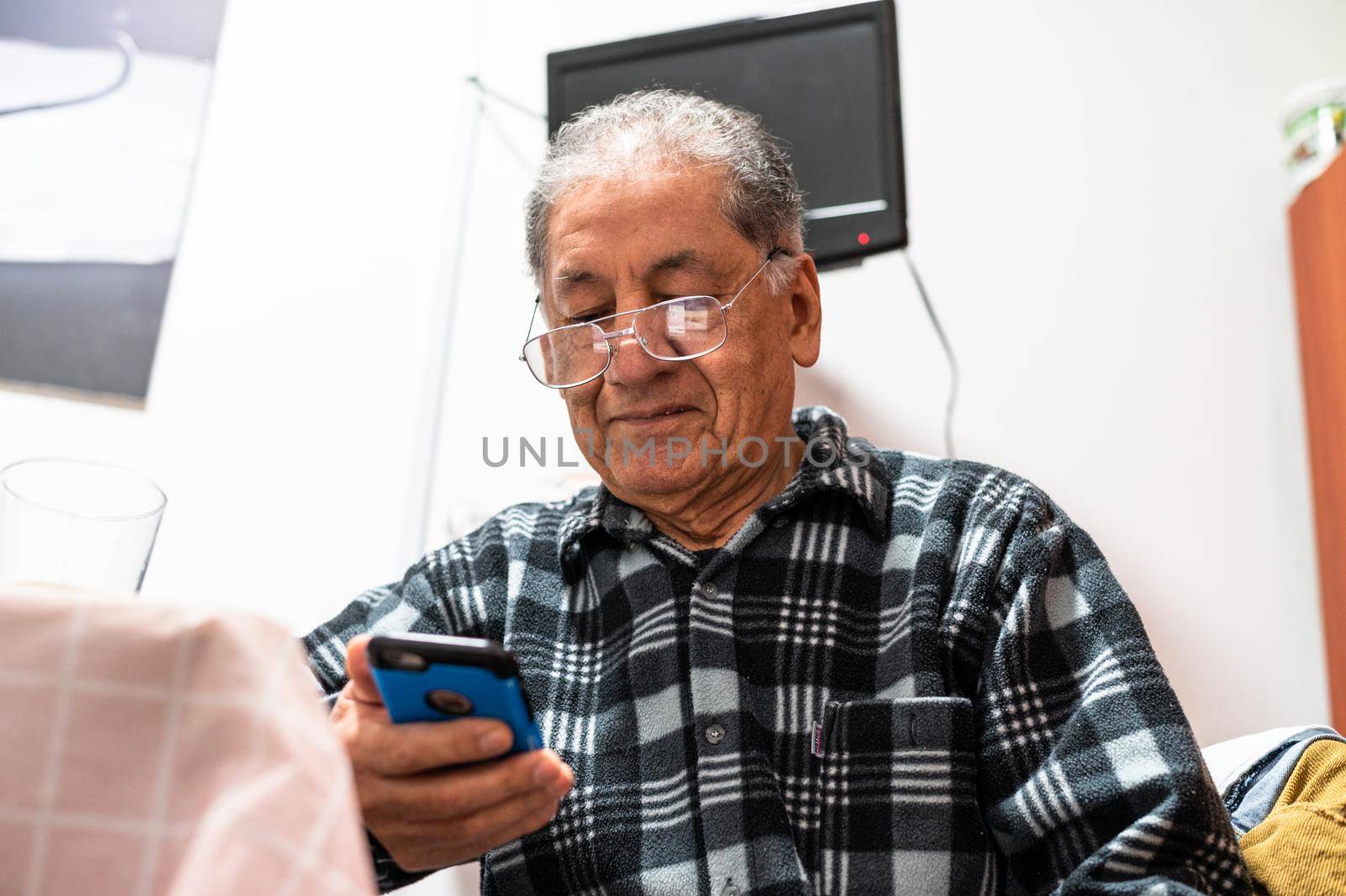 Happy senior Caucasian man in glasses look at cellphone screen browse wireless internet. Smiling modern mature 70s grandfather text or message on smartphone. Elderly use cell technologies at home. by Peruphotoart