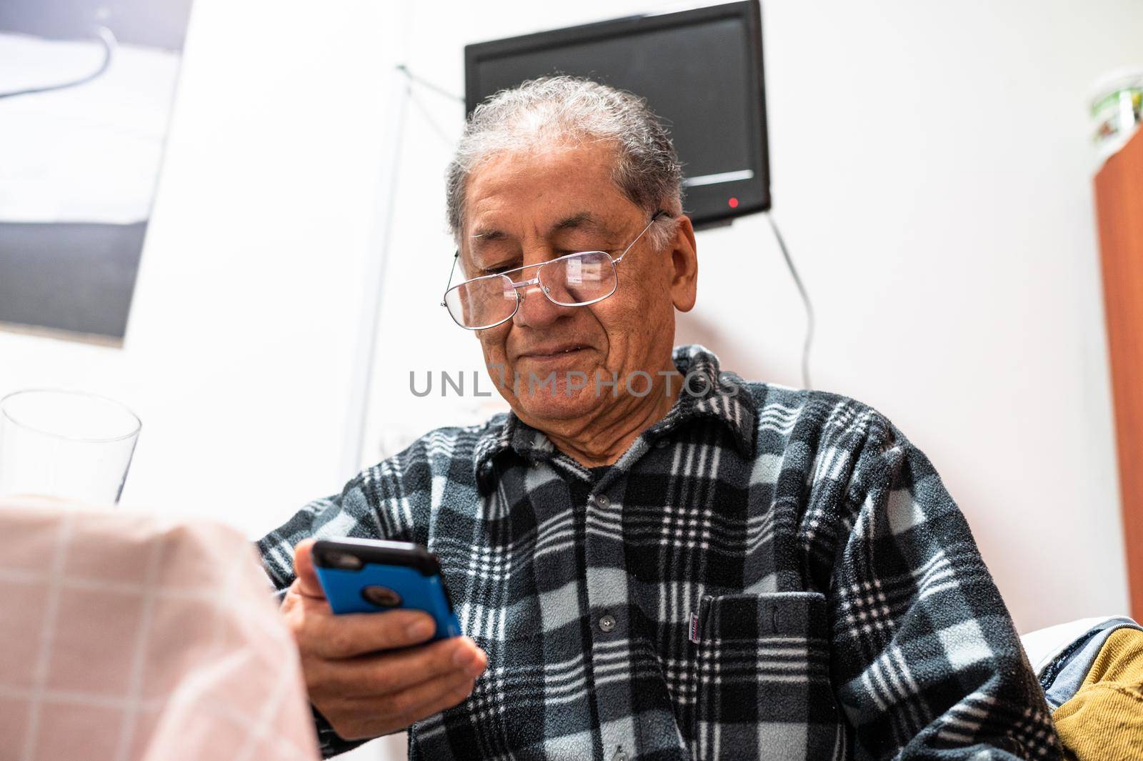 Happy senior Caucasian man in glasses look at cellphone screen browse wireless internet. Smiling modern mature 70s grandfather text or message on smartphone. Elderly use cell technologies at home.