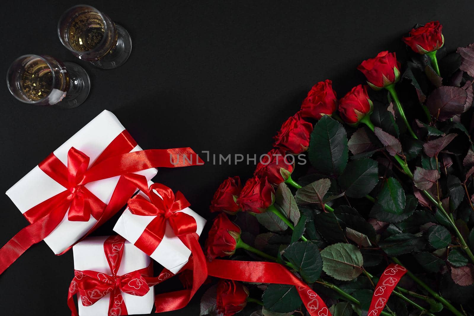 Valentines day greeting card. Red rose flowers, champagne and gift boxex on black table. Top view with copy space. Still life. Flat lay