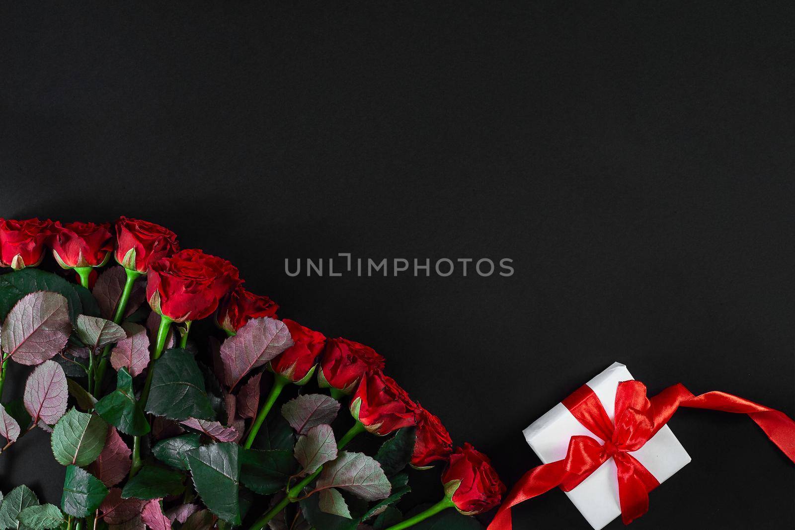 Red roses and white gift box with red ribbon on black background by nazarovsergey