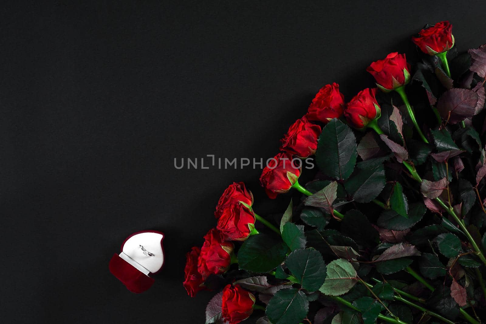 A bouquet of red roses and a box of ring on black background. View top. Flat lay. Copy space. Still life Valentine's Day