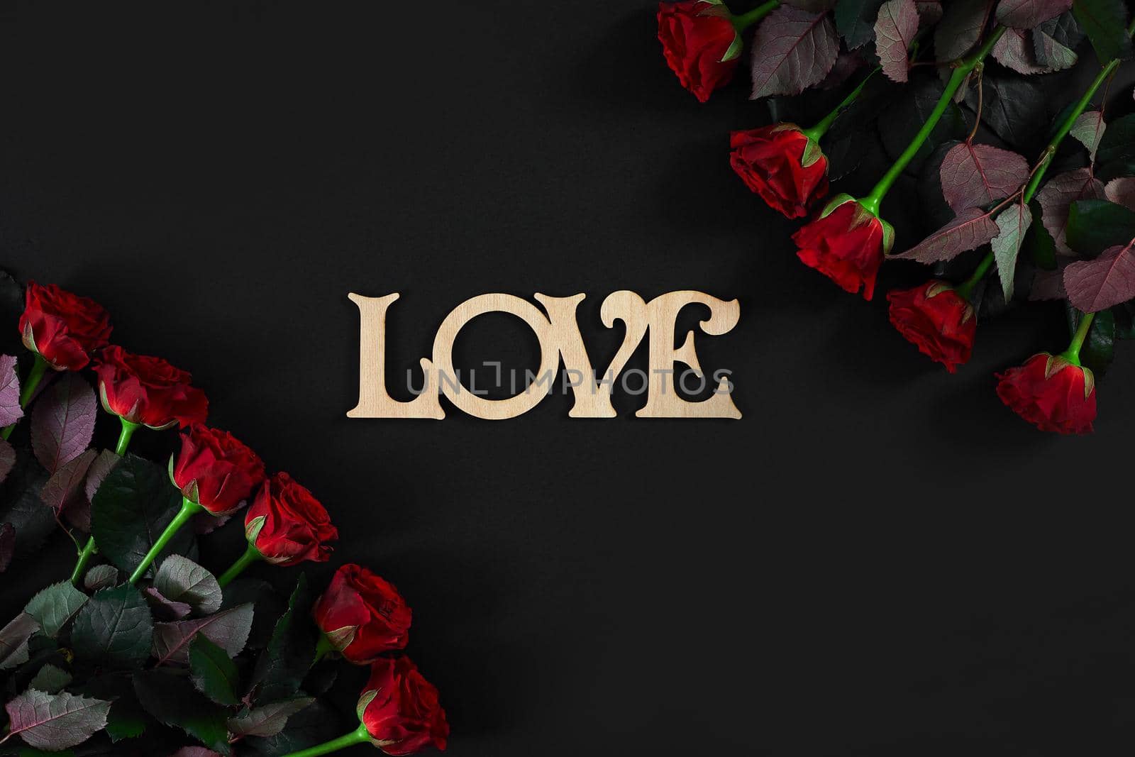 Red roses flowers with wooden word LOVE on black background with place for text. Romantic Valentines holidays concept. Valentine's day greeting card.. Copy space. Still life. Flat lay