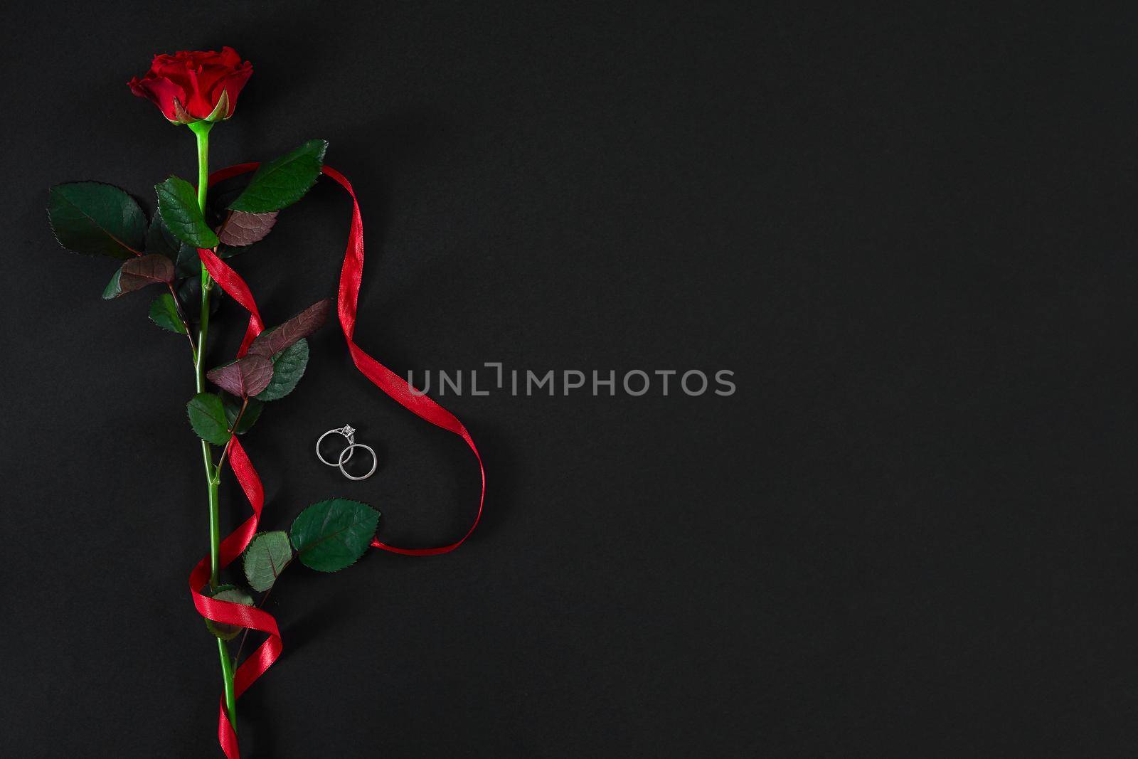 One dark red rose with red ribbon and the ring on black backgrou by nazarovsergey