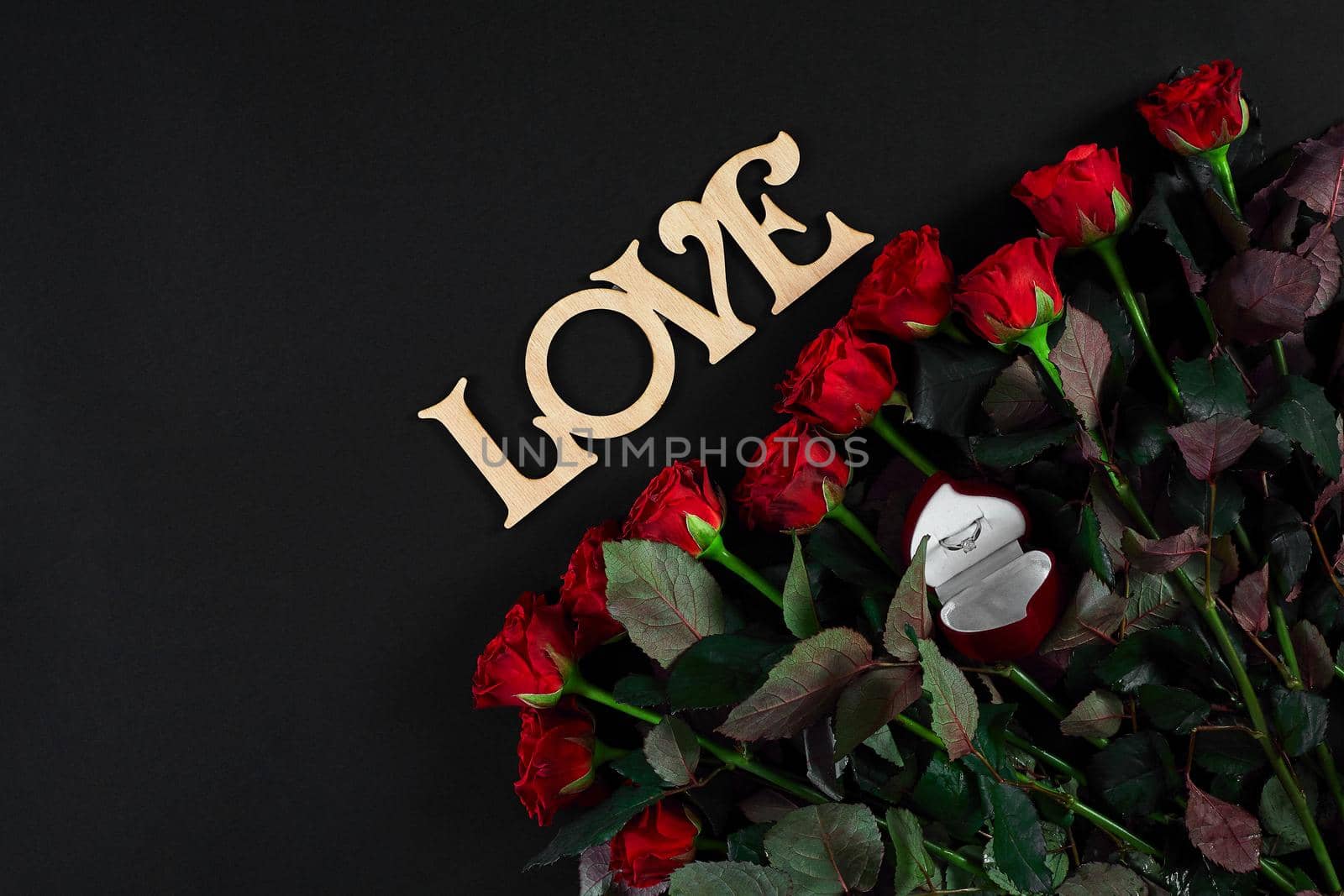 Red roses, ring and gift box on black background. Top view. Flat lay. Copy space. Still life