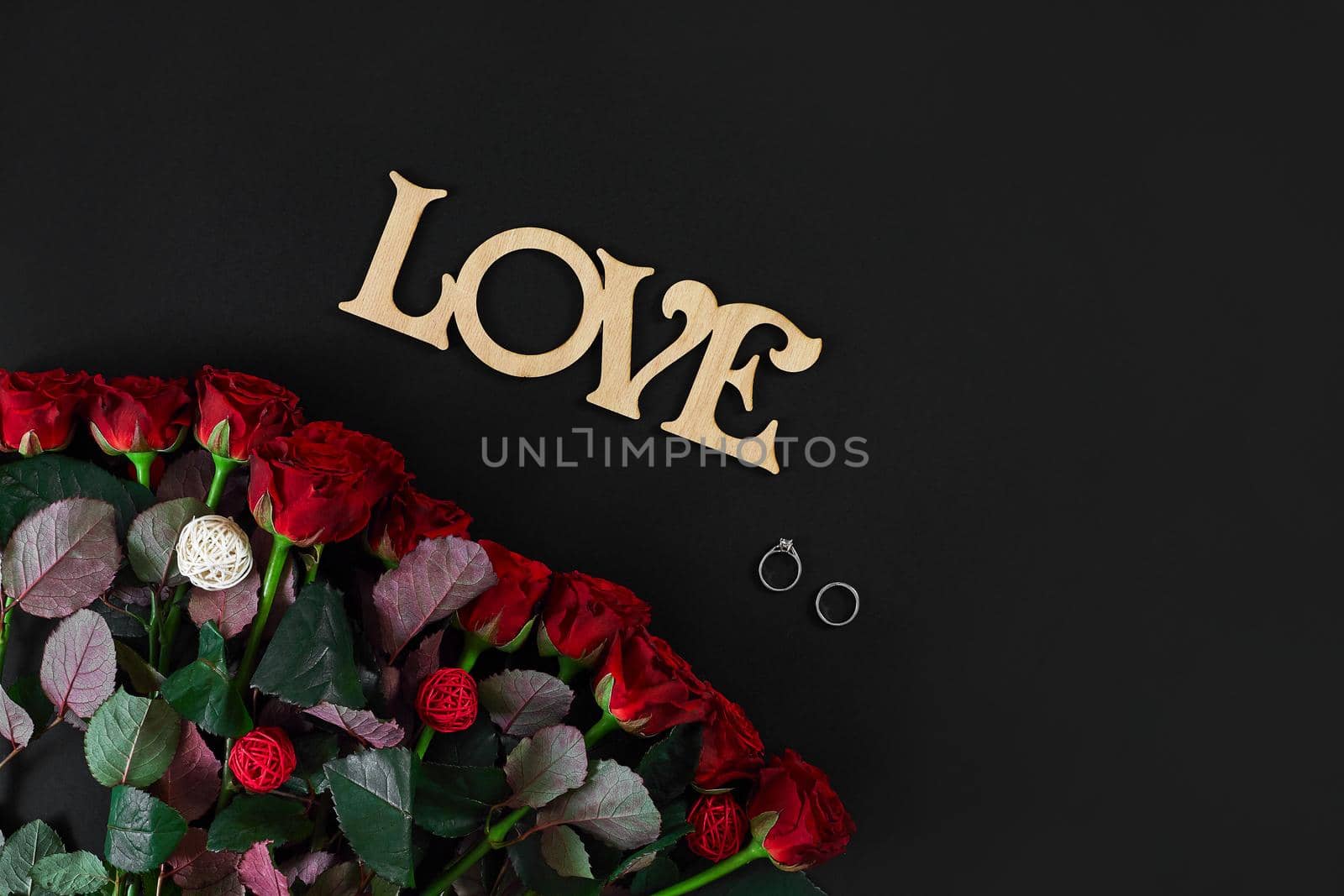 Red roses flowers with wooden word LOVE on black background with place for text. Romantic Valentines holidays concept. Valentine's day greeting card.. Copy space. Still life. Flat lay