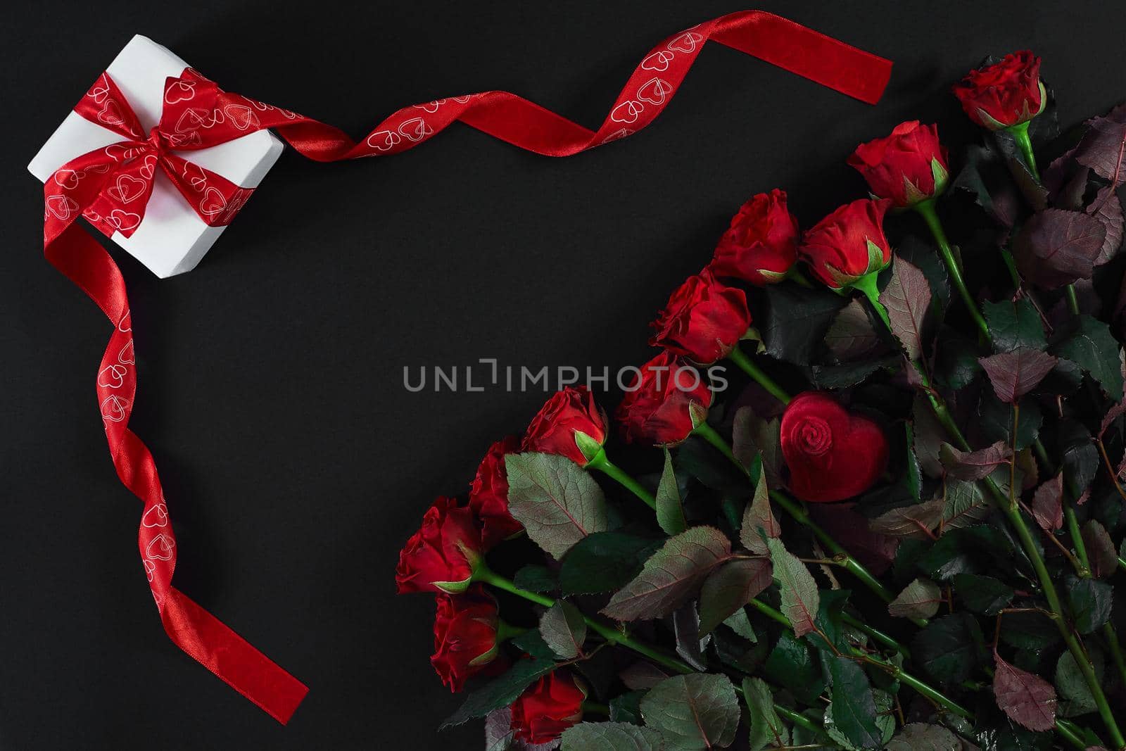 Red roses and gift box on black background. Top view. Flat lay. Copy space. Still life Valentine's Day