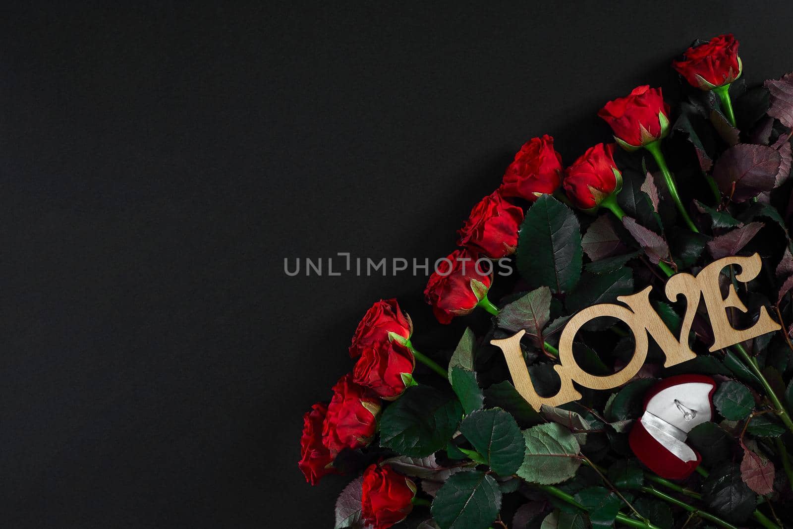 A bouquet of red roses and a box of ring on black background. View top. Flat lay. Copy space. Still life