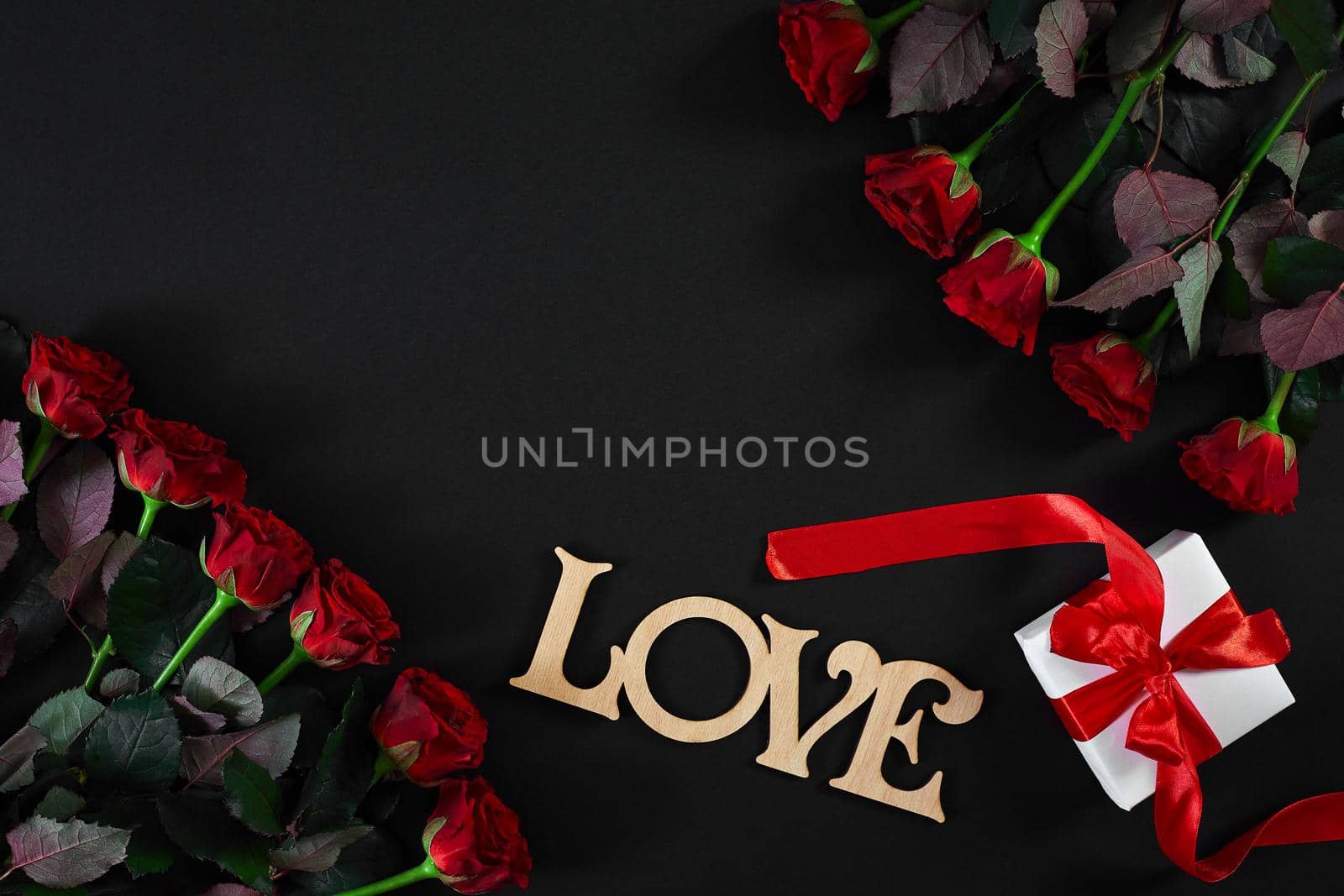 Red roses flowers with wooden word LOVE on black background with place for text. Romantic Valentines holidays concept. Valentine's day greeting card.. Copy space. Still life. Flat lay