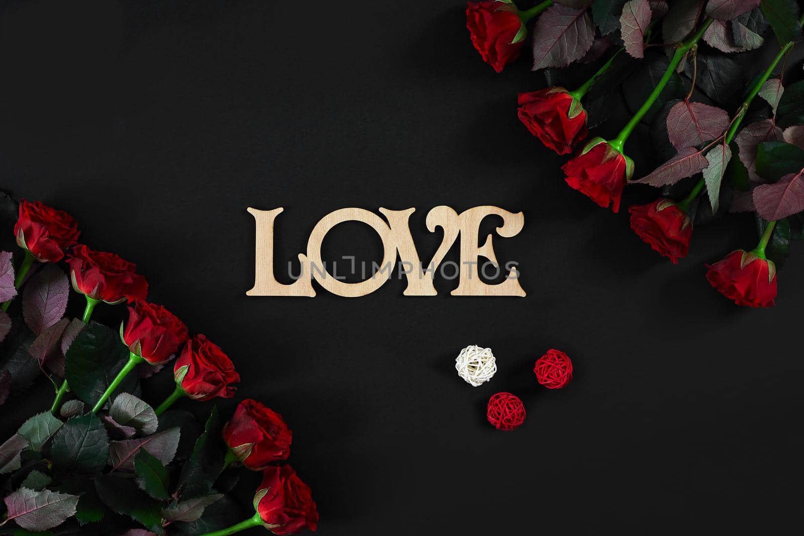 Red roses flowers with wooden word LOVE on black background with place for text. Romantic Valentines holidays concept. Valentine's day greeting card. Copy space. Still life. Flat lay